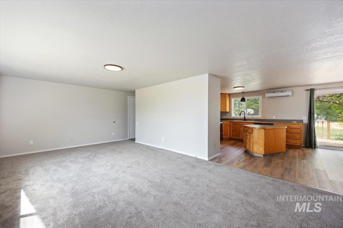 Unfurnished living room with dark carpet, healthy amount of natural light, a wall unit AC, and a textured ceiling