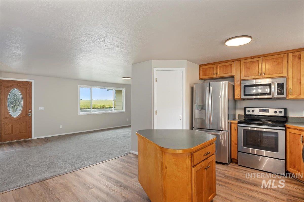 Kitchen with stainless steel appliances, a kitchen island, open floor plan, light wood-style floors, and brown cabinetry