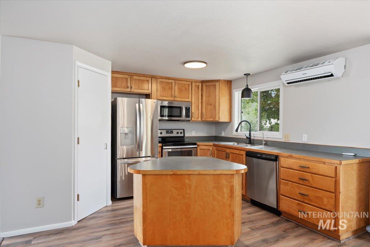 Kitchen with stainless steel appliances, a wall mounted AC, light wood-type flooring, a center island, and decorative light fixtures
