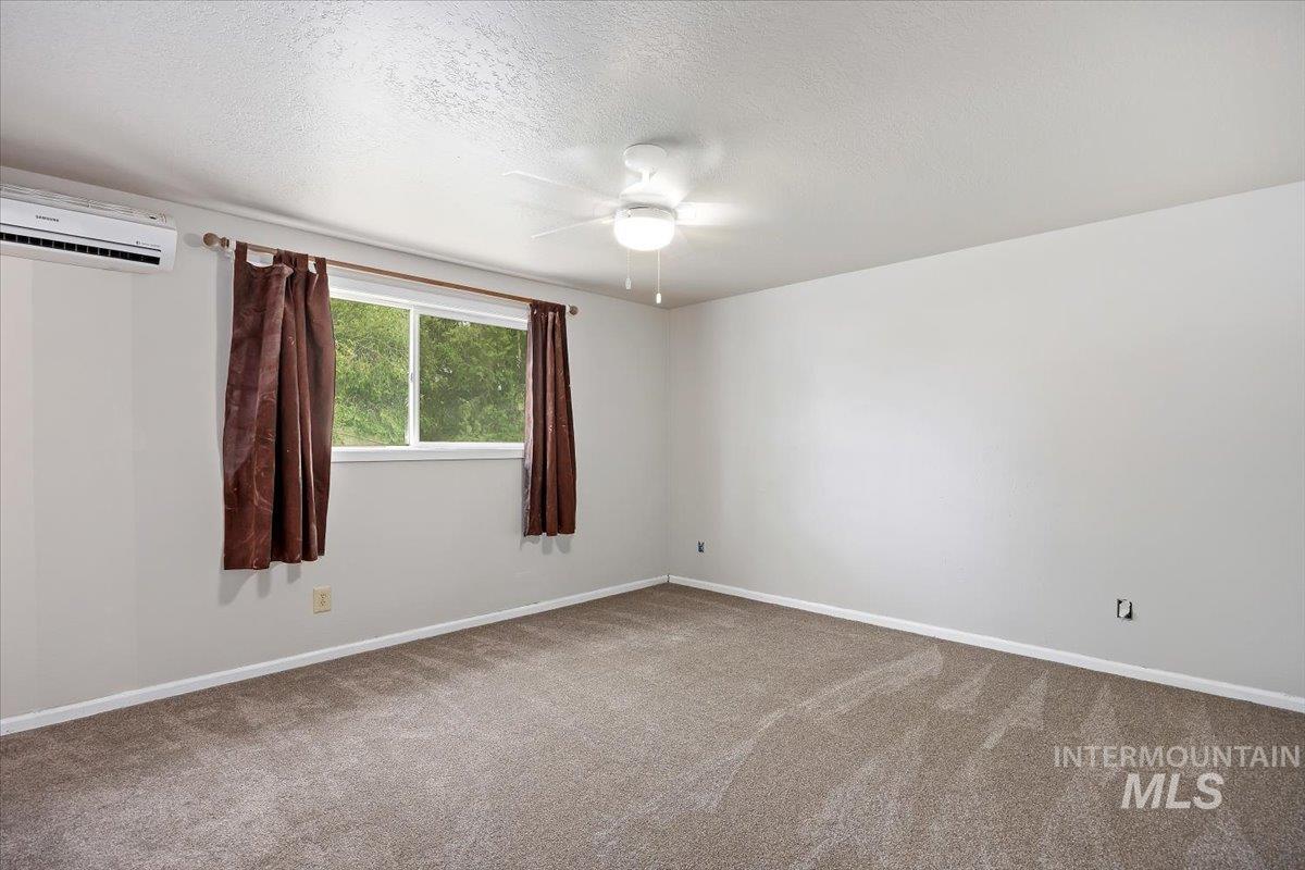 Unfurnished room with a wall mounted AC, carpet floors, a textured ceiling, and ceiling fan
