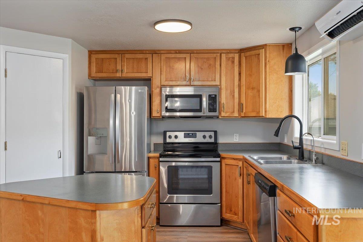 Kitchen with stainless steel appliances, a wall mounted air conditioner, light wood-style flooring, pendant lighting, and brown cabinets