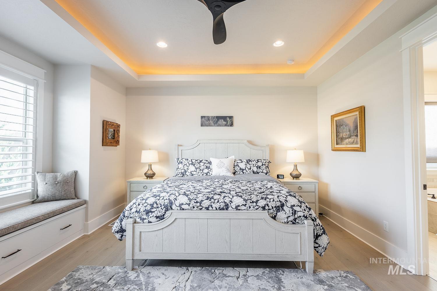 Bedroom featuring a raised ceiling, light wood-style floors, a ceiling fan, recessed lighting, and ensuite bath