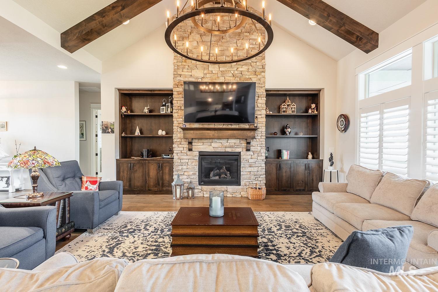 Living room with a fireplace, high vaulted ceiling, wood finished floors, built in shelves, and a chandelier