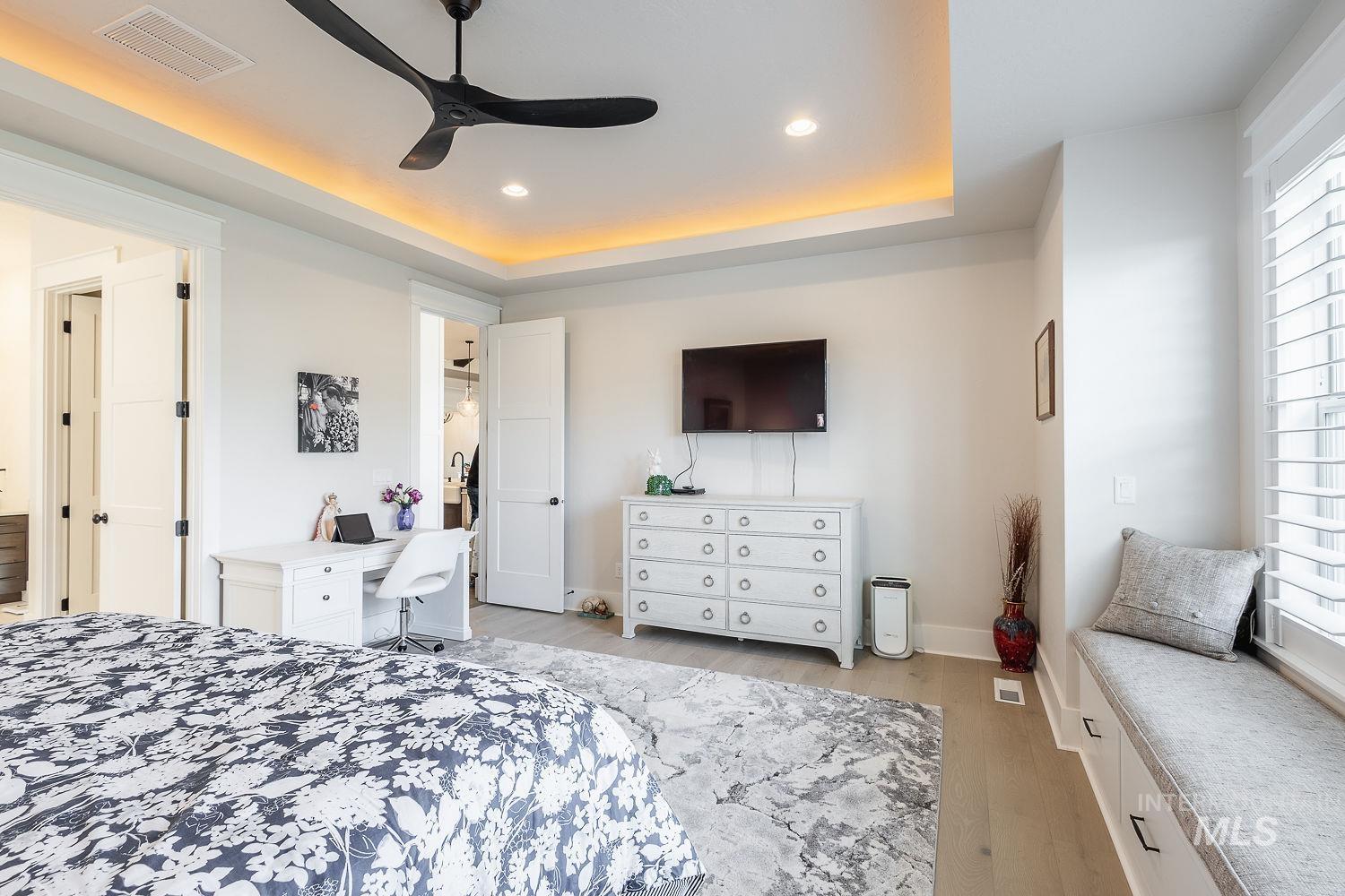 Bedroom with a raised ceiling, light wood-style floors, a ceiling fan, a desk, and recessed lighting