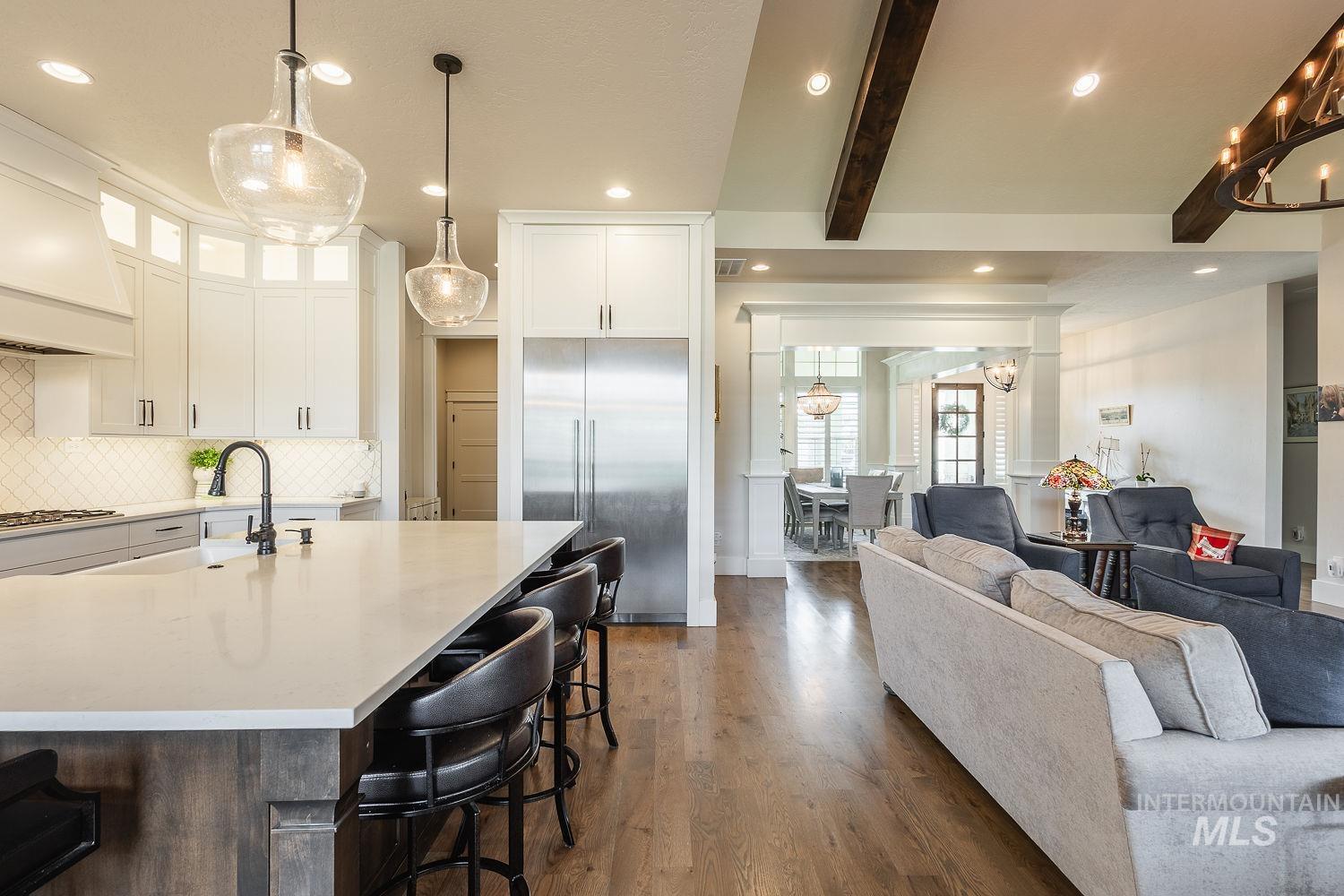 Kitchen with hanging light fixtures, beamed ceiling, built in refrigerator, a kitchen breakfast bar, and white cabinetry