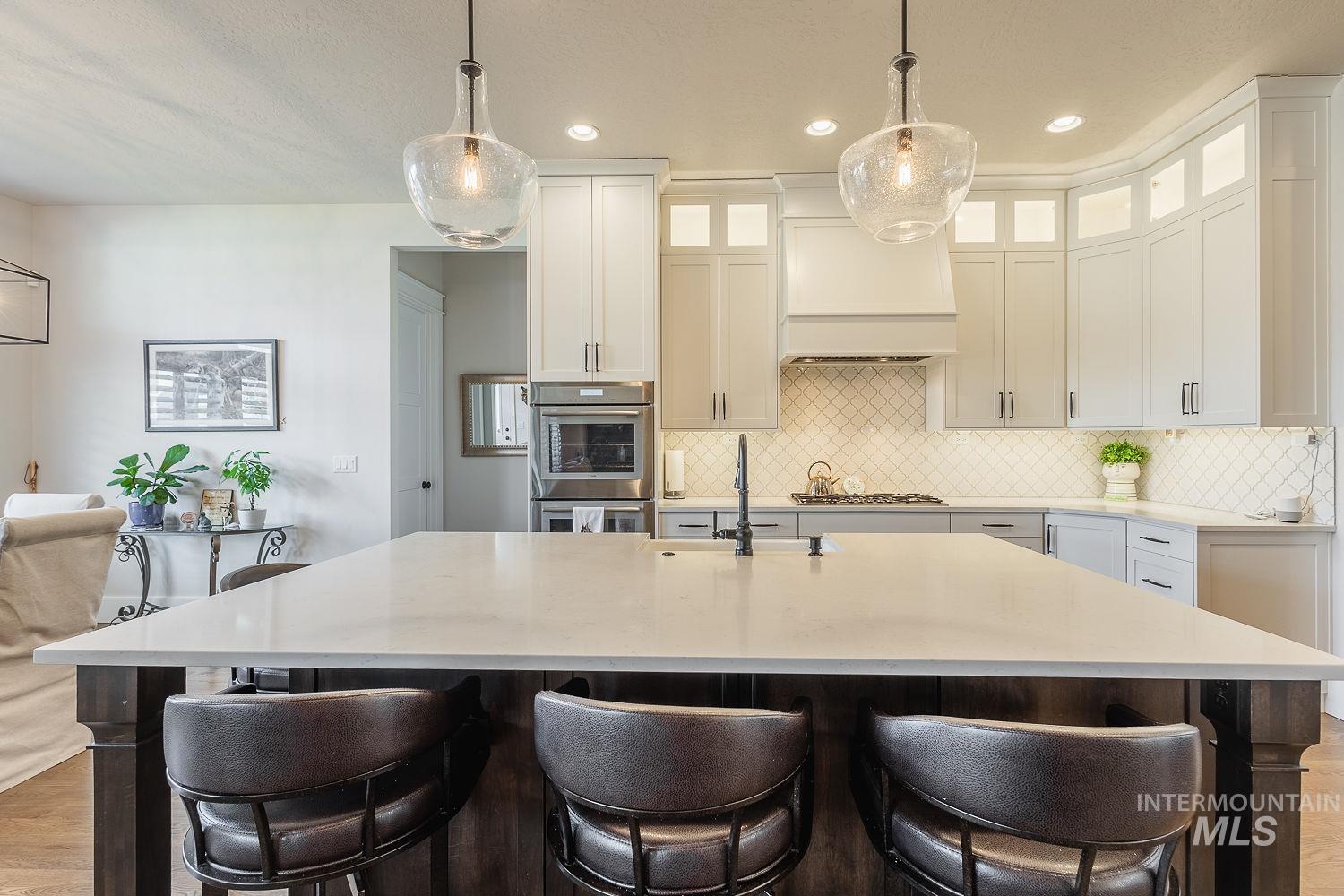 Kitchen with pendant lighting, light stone counters, glass insert cabinets, a kitchen breakfast bar, and recessed lighting