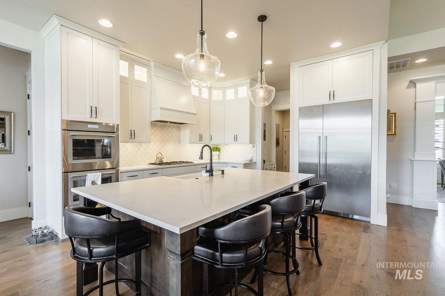 Kitchen with a breakfast bar area, glass insert cabinets, stainless steel appliances, a kitchen island with sink, and white cabinets