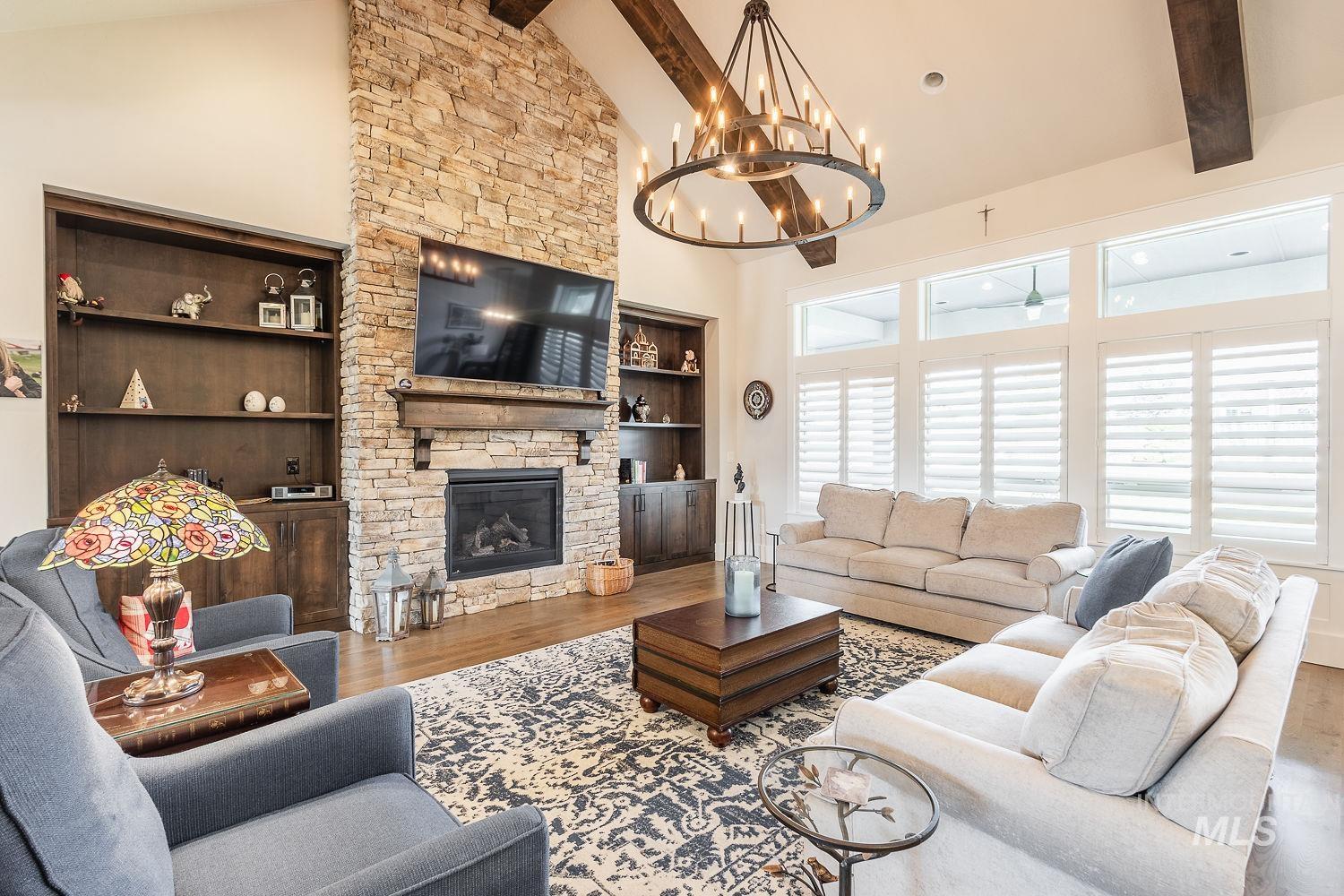 Living area featuring high vaulted ceiling, beam ceiling, a fireplace, a chandelier, and wood finished floors