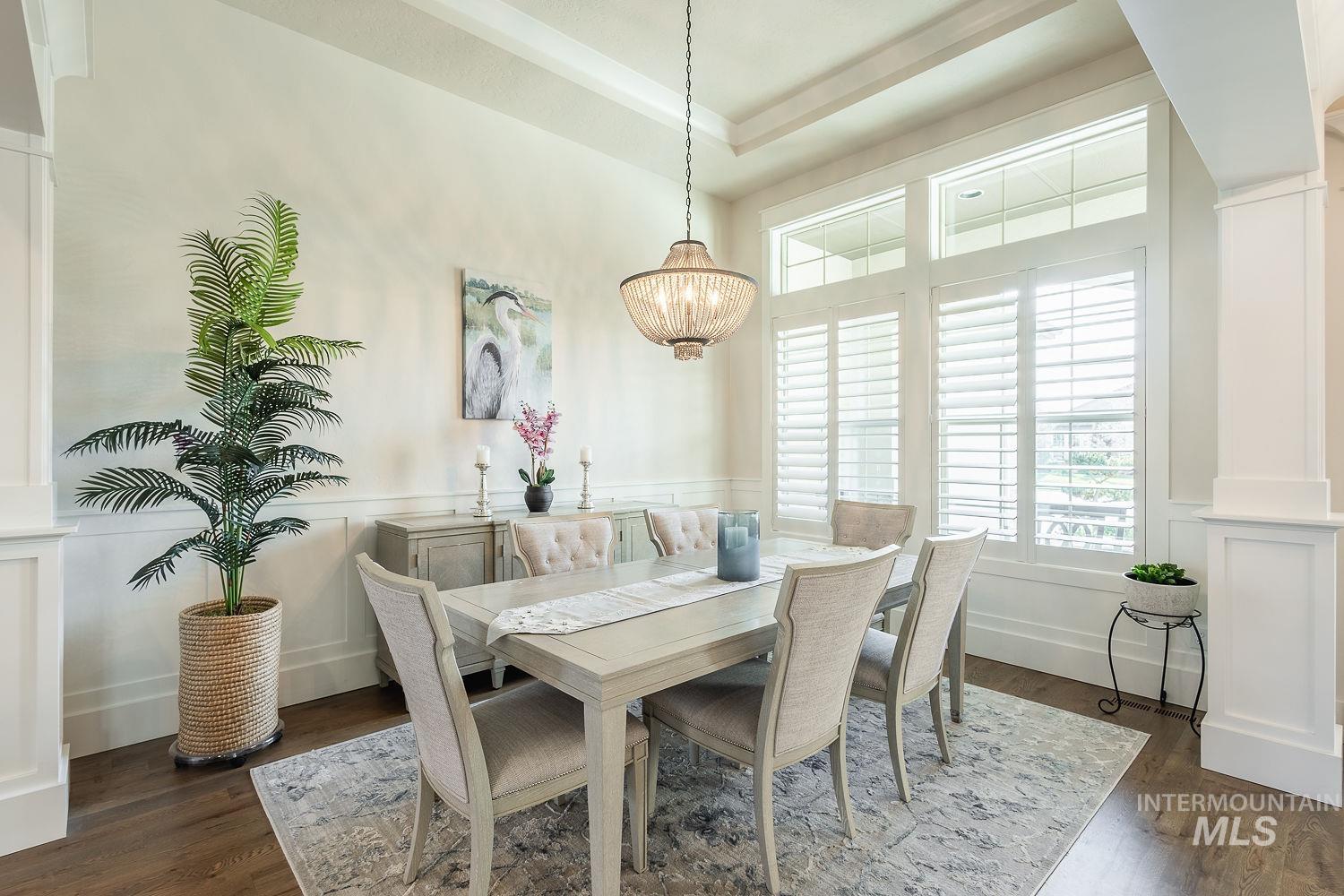 Dining space featuring dark wood finished floors, wainscoting, a decorative wall, and a raised ceiling