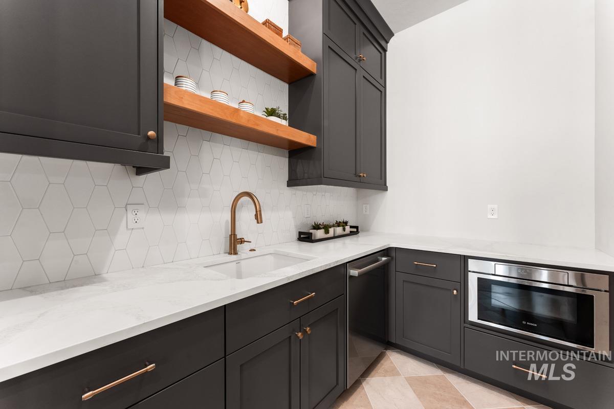 Kitchen with light stone counters, stainless steel appliances, dark cabinetry, open shelves, and backsplash