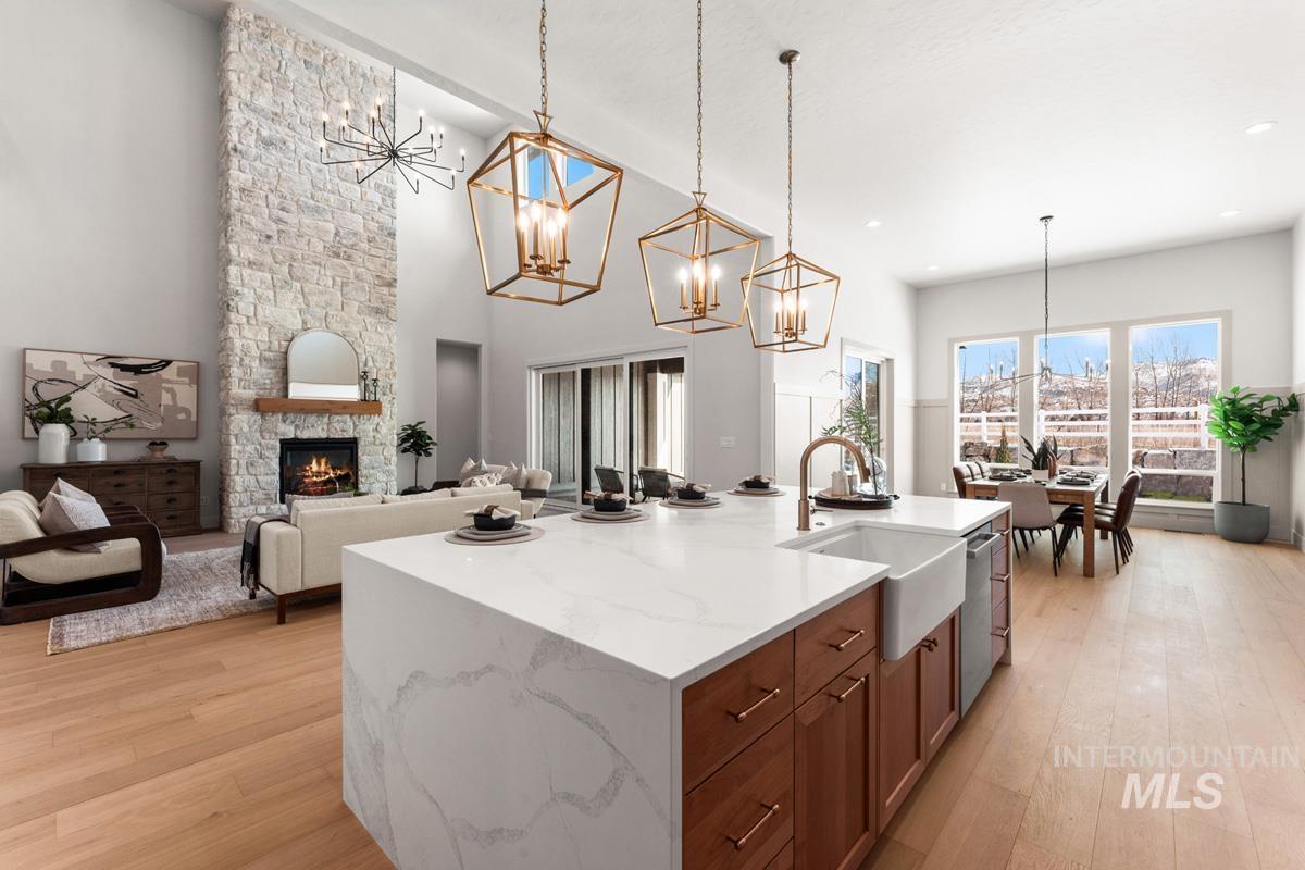 Kitchen with a stone fireplace, a chandelier, open floor plan, an island with sink, and a high ceiling