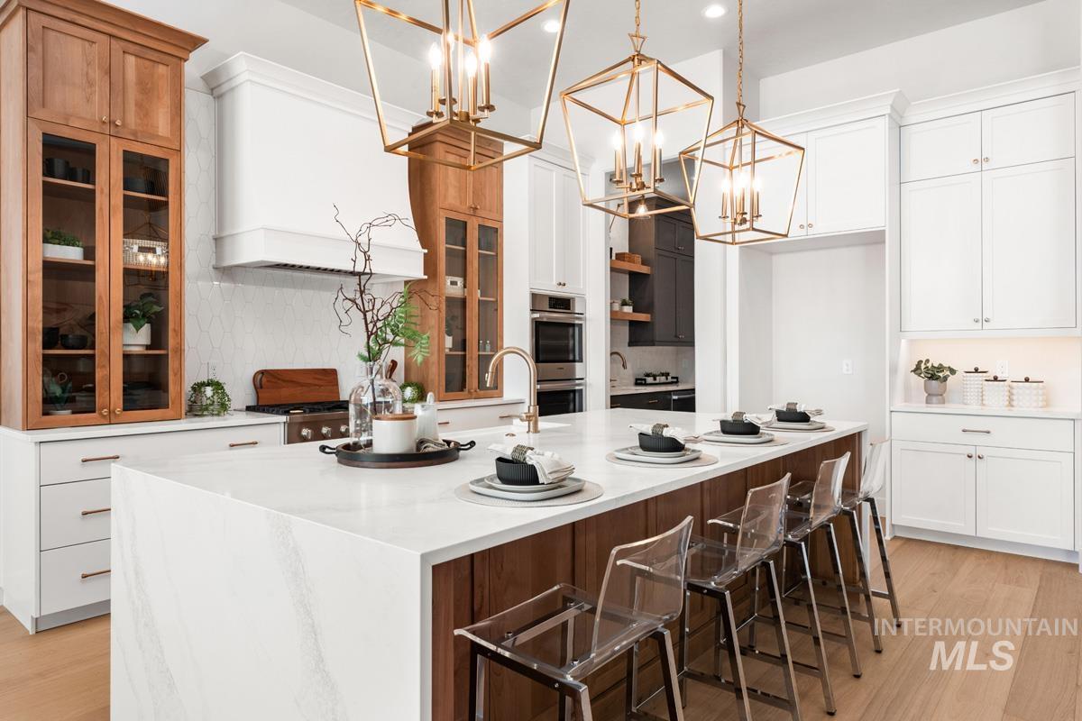Dual tone kitchen with light wood finished floors, a kitchen bar, glass fronted cabinets, light stone countertops, and dual tone cabinetry