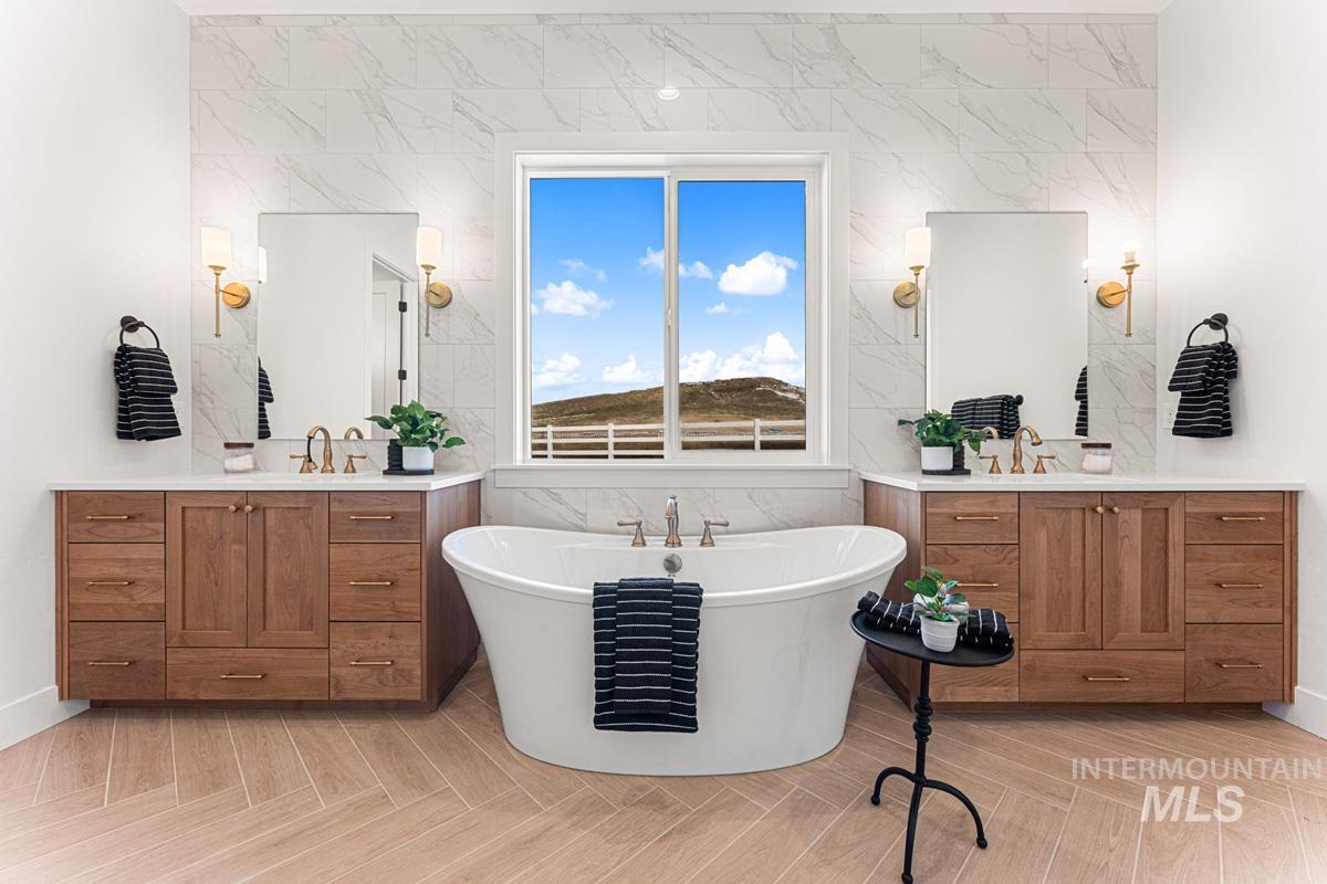 Full bathroom with two vanities, a freestanding tub, and light wood-style flooring