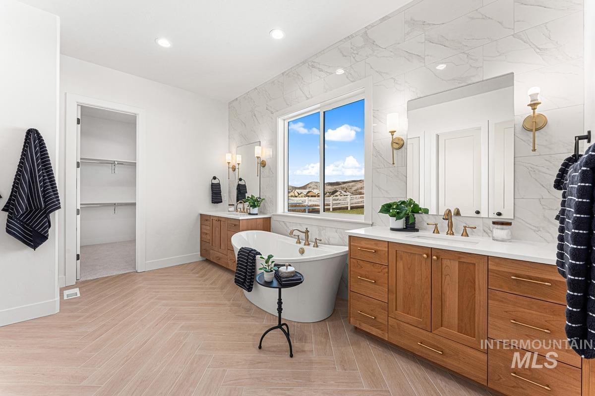 Full bathroom with two vanities, a walk in closet, a soaking tub, parquet floors, and recessed lighting