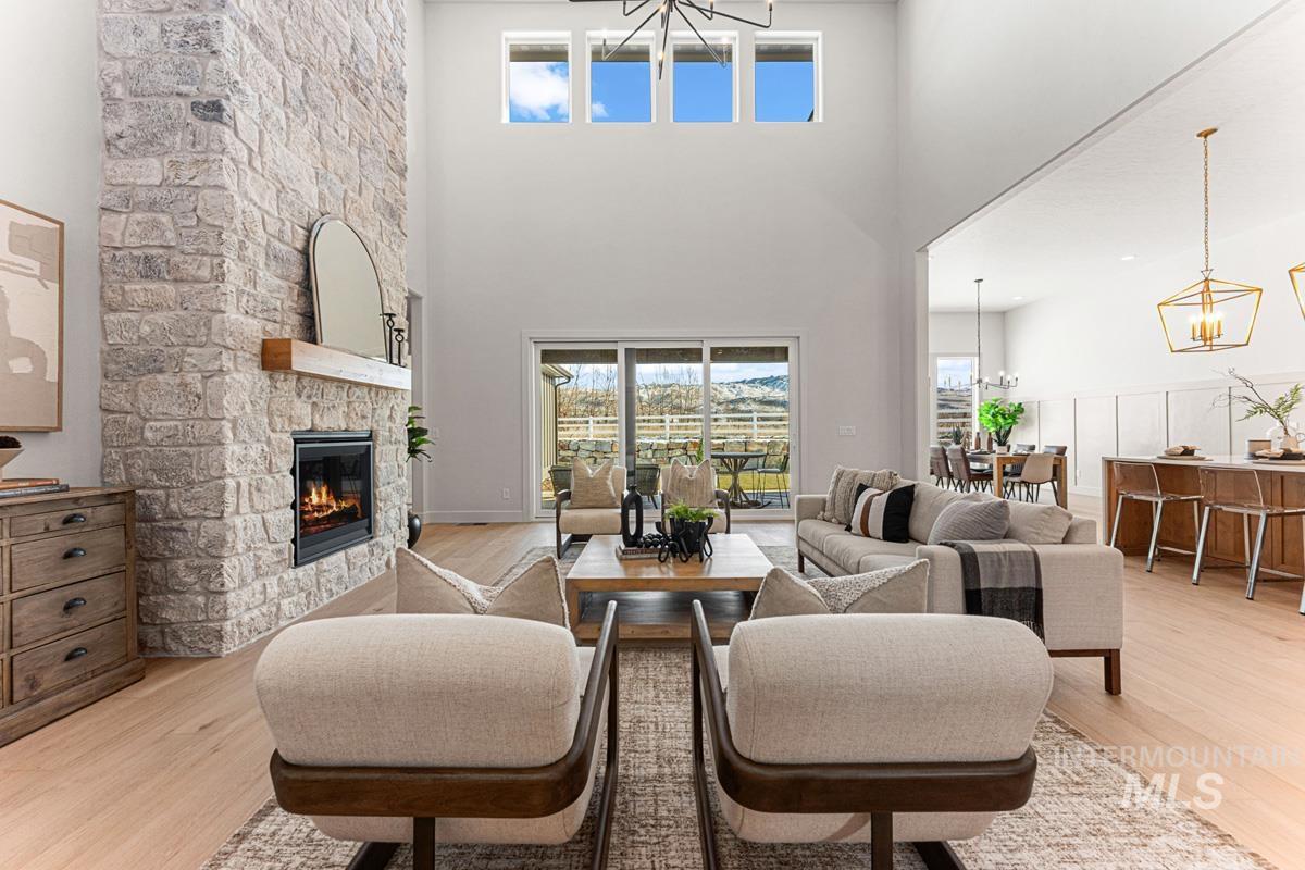 Living area with suspended lighting, a stone fireplace, light wood-style flooring, and a high ceiling