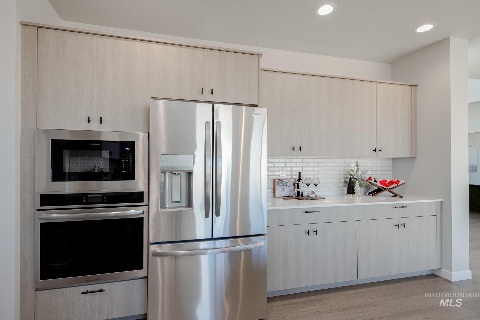 Kitchen with appliances with stainless steel finishes, recessed lighting, backsplash, light stone countertops, and light wood-type flooring