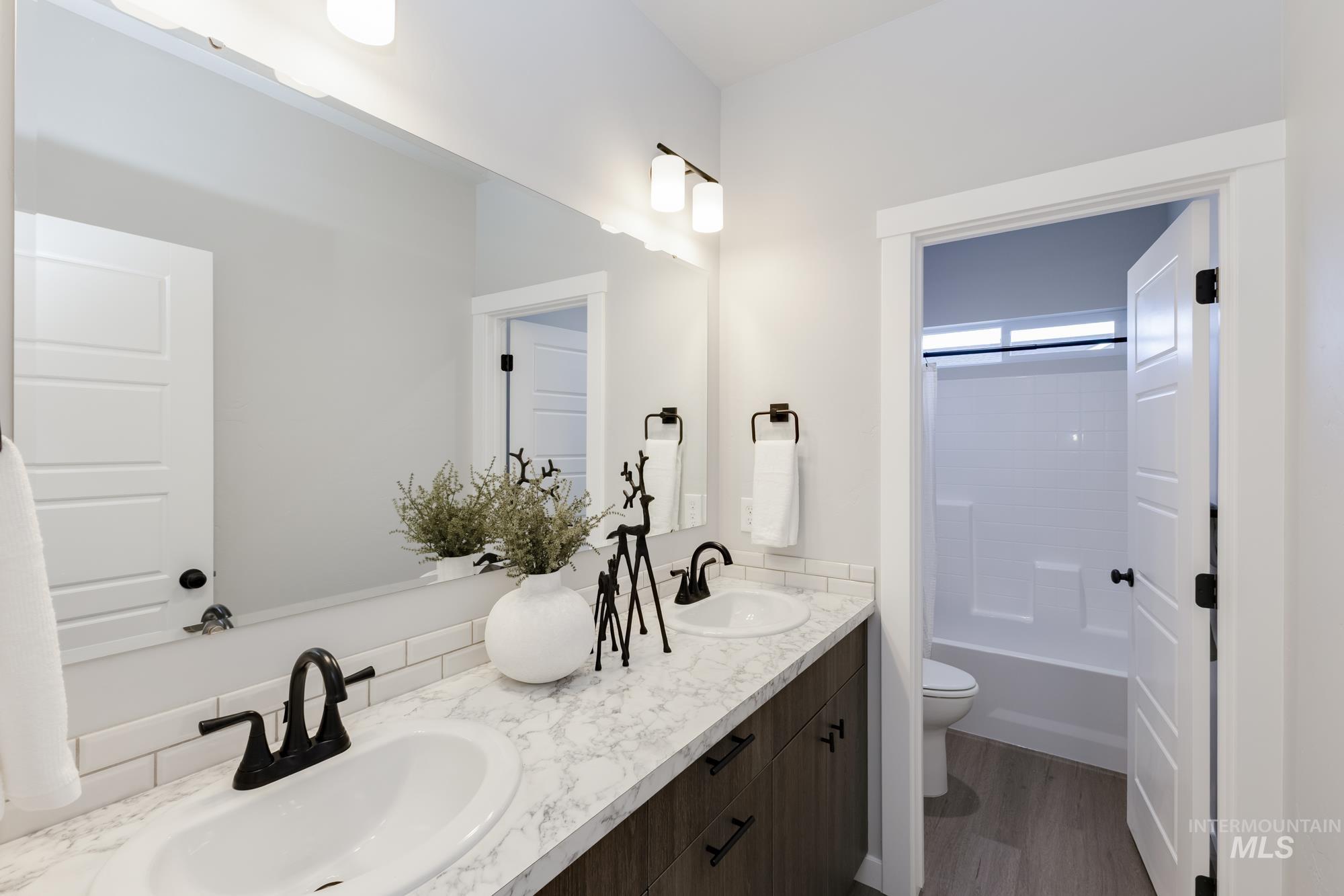 Full bath featuring double vanity, dark wood-style flooring, and shower / bath combination