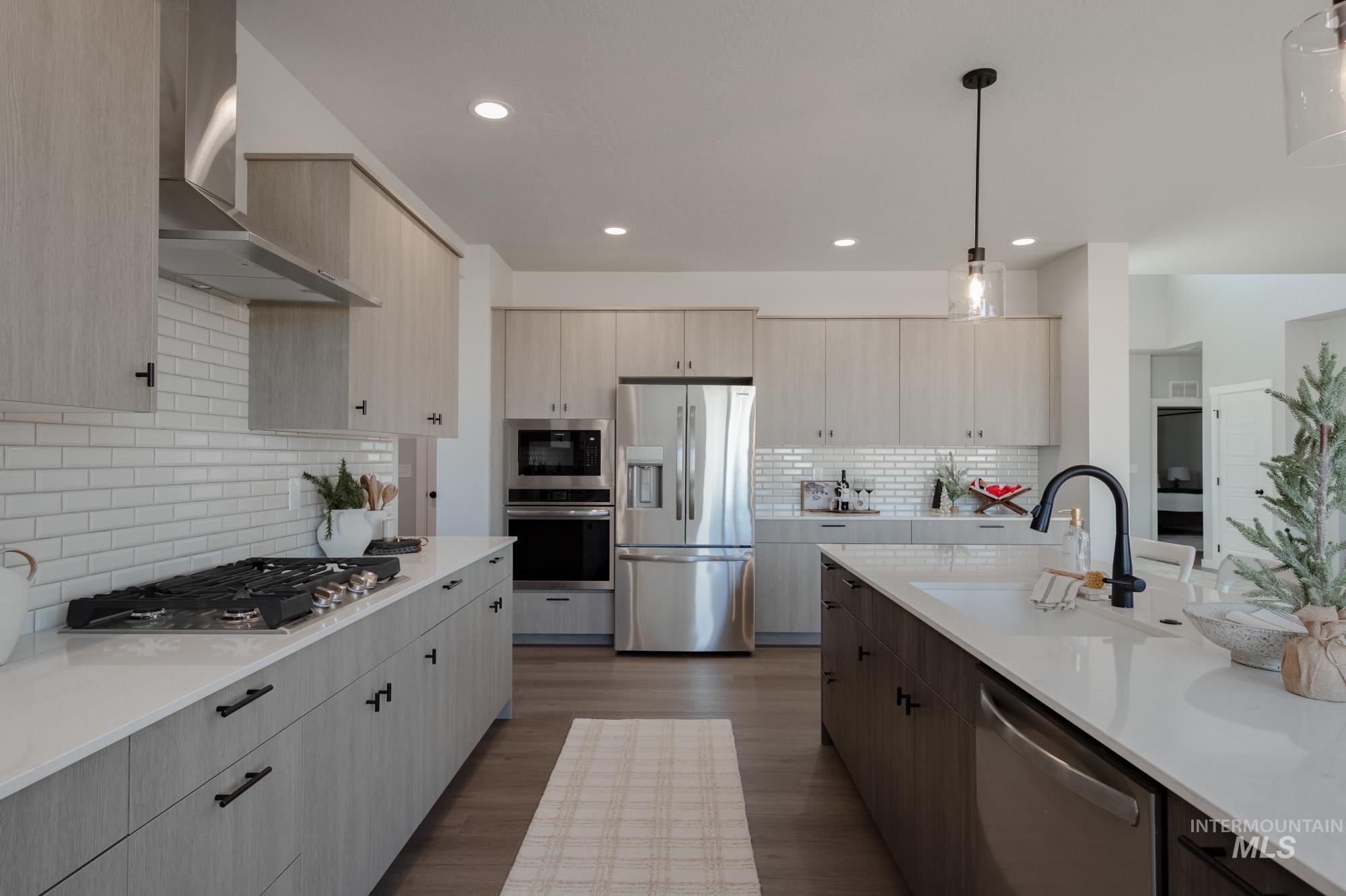 Kitchen featuring appliances with stainless steel finishes, wall chimney exhaust hood, hanging light fixtures, dark wood-type flooring, and tasteful backsplash