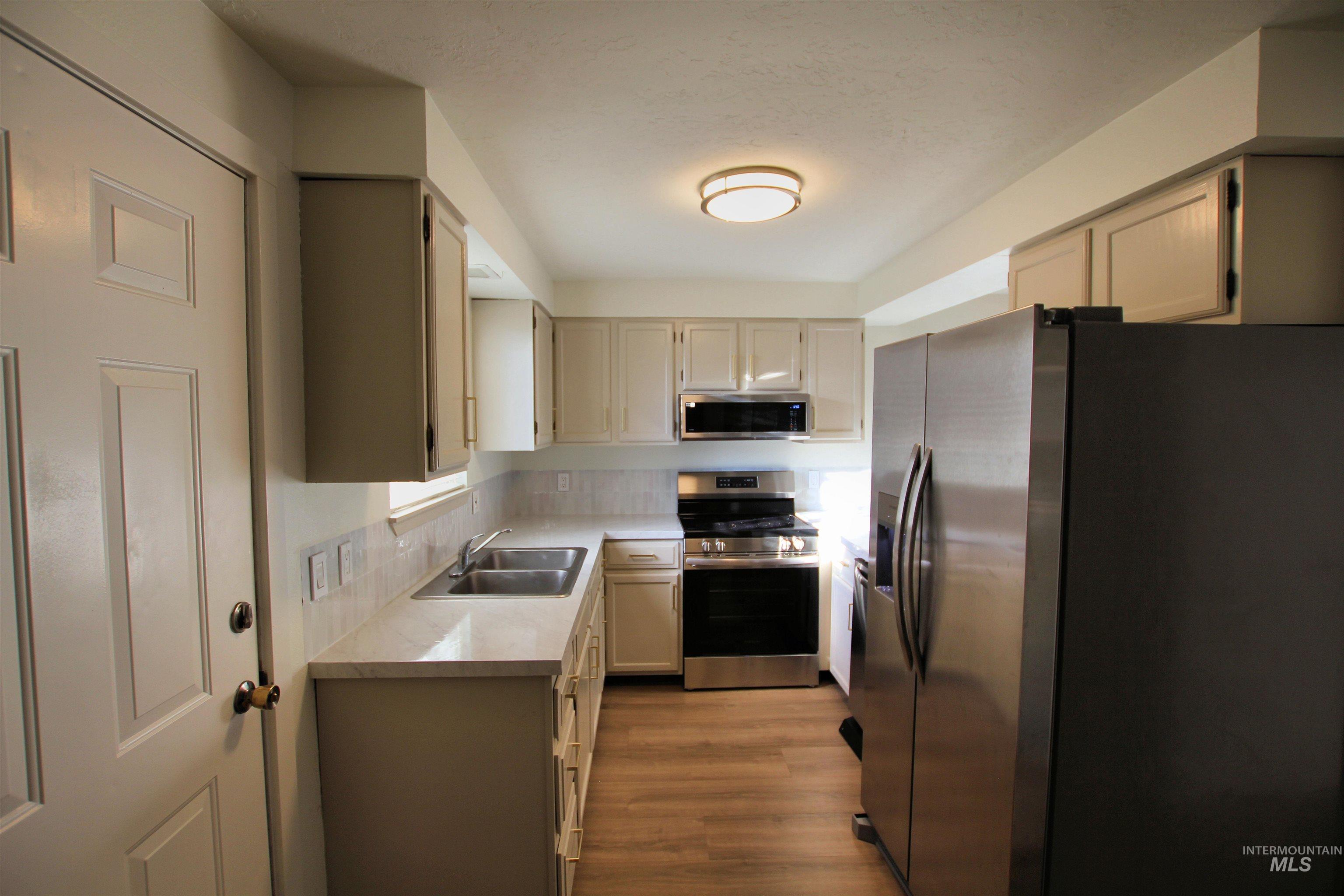 Kitchen with stainless steel appliances, light countertops, light wood-style floors, and backsplash