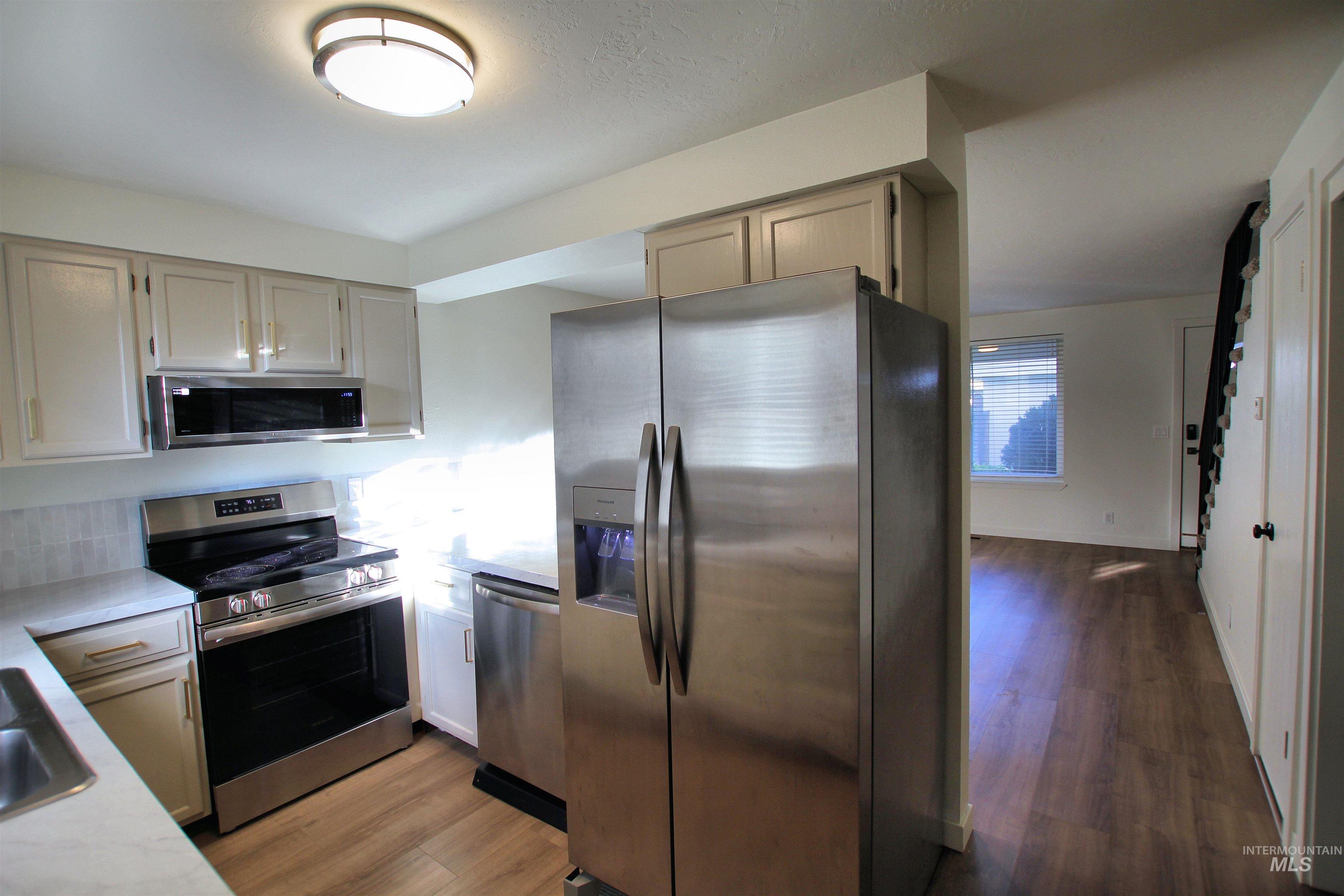 Kitchen featuring appliances with stainless steel finishes, dark wood-type flooring, and light stone countertops