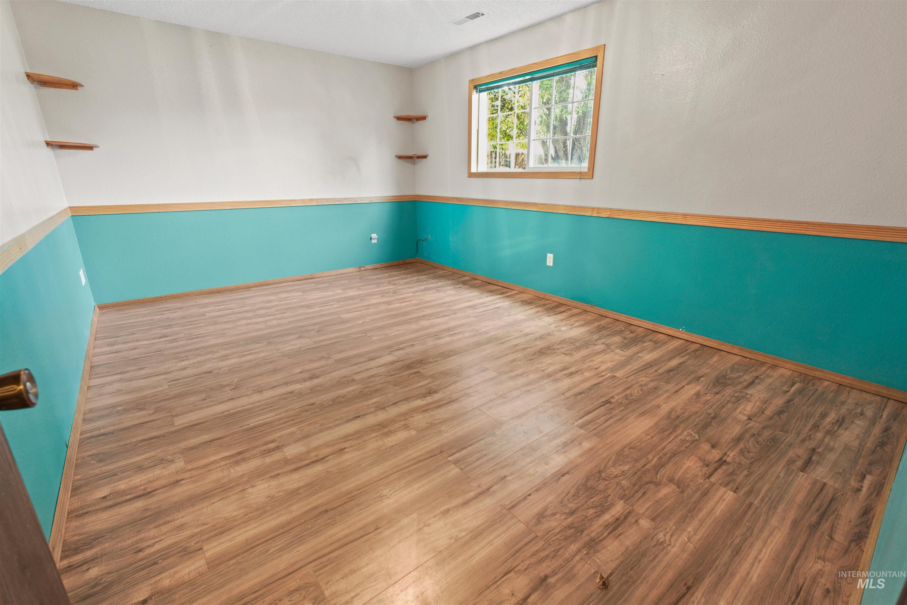 Room featuring wood-finish flooring, a window with exterior views, and accent shelving