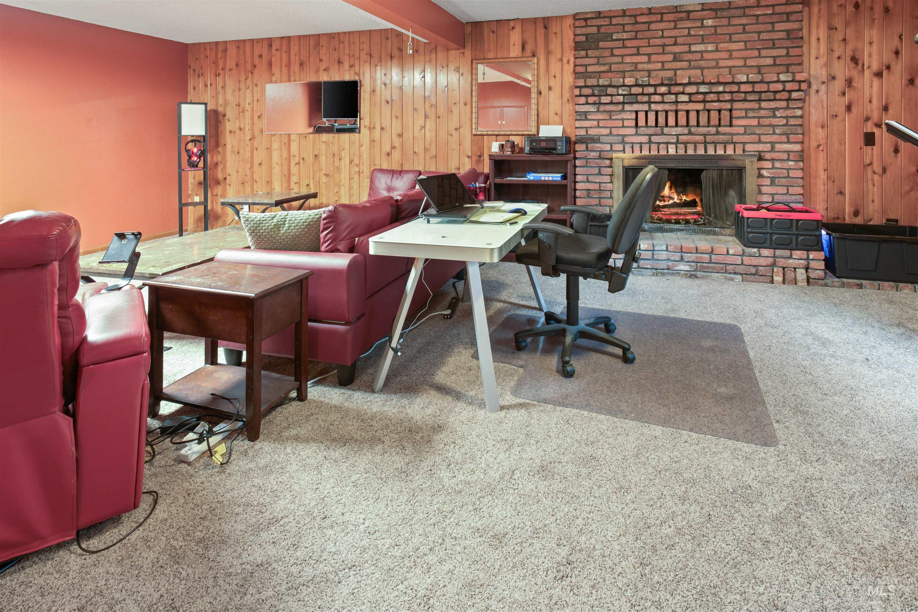 Living space featuring a brick fireplace with a raised hearth, wood-paneled walls, and carpet flooring