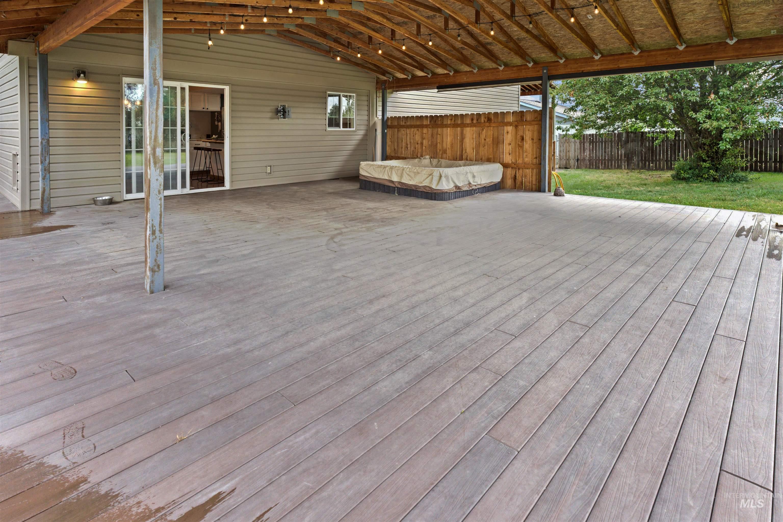 Expansive covered patio featuring wood-finish decking, exposed beam ceiling, string lighting, and direct access to the interior via sliding glass doors