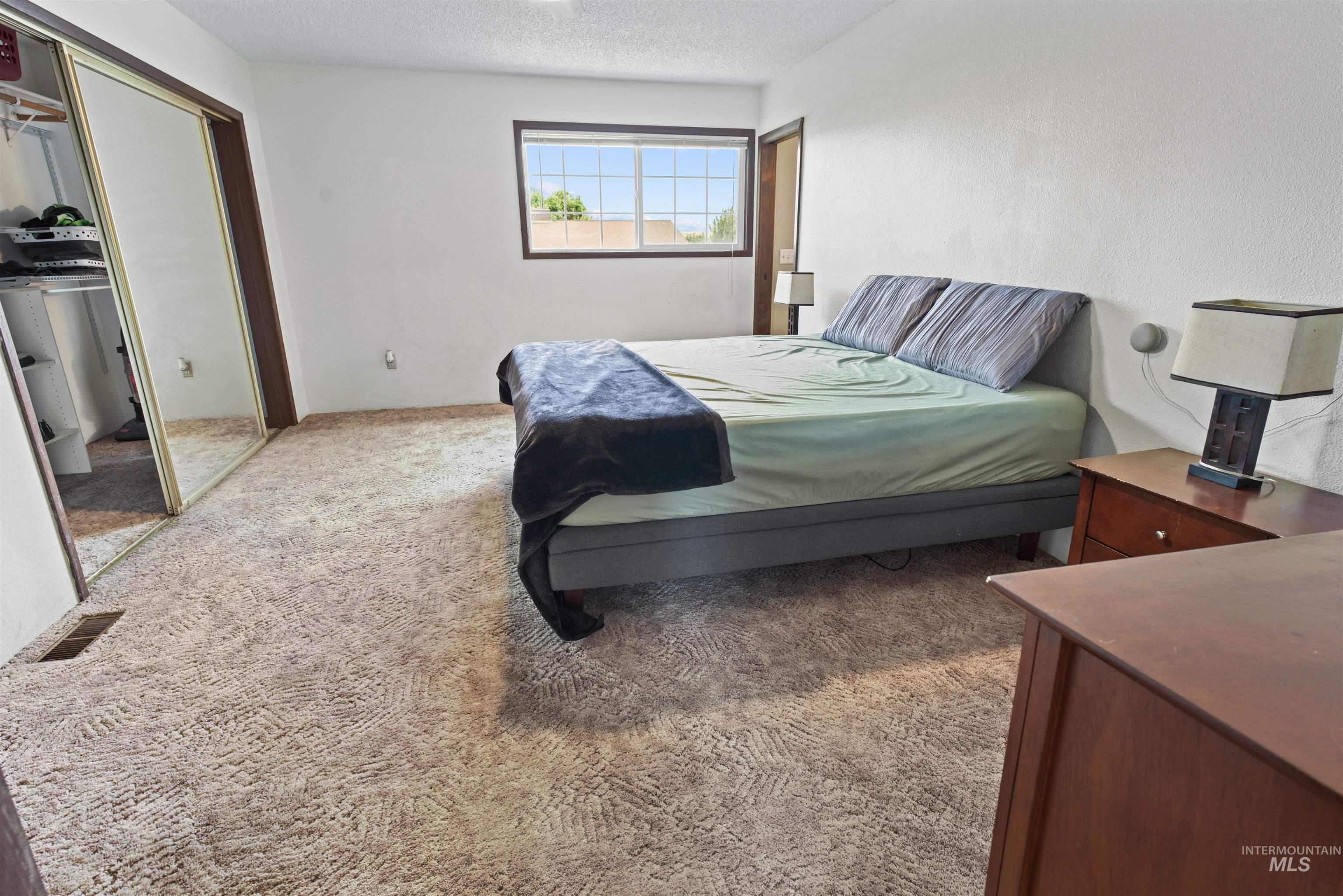 Bedroom with light-colored carpet, a window, and a mirrored closet door