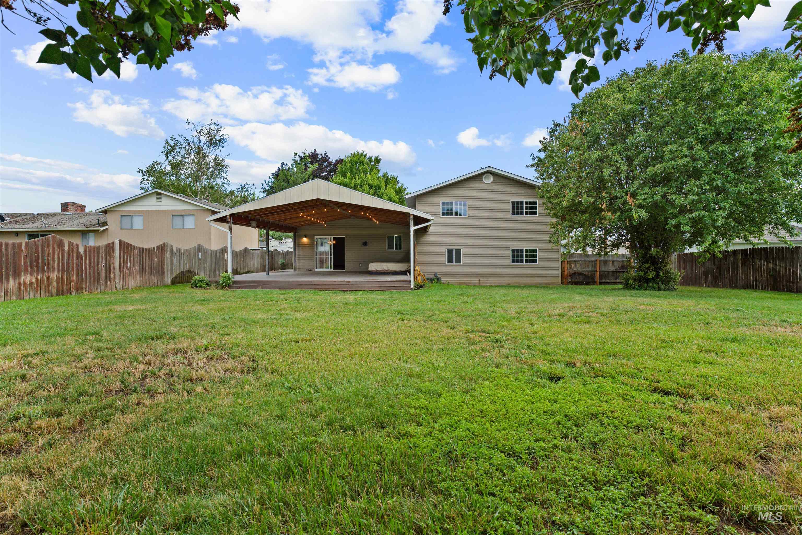 Expansive backyard featuring a covered patio with string lighting, a large wood deck, and a mature shade tree