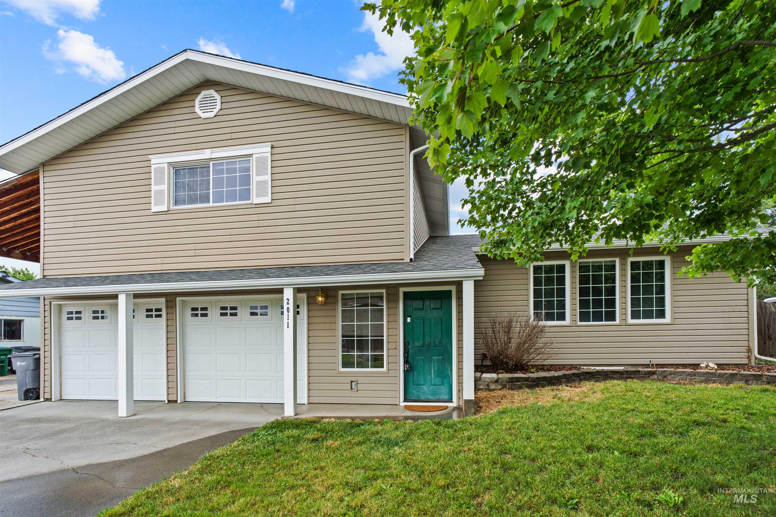 Two-story residence featuring tan siding, a teal entry door, and a white-trimmed window with shutters