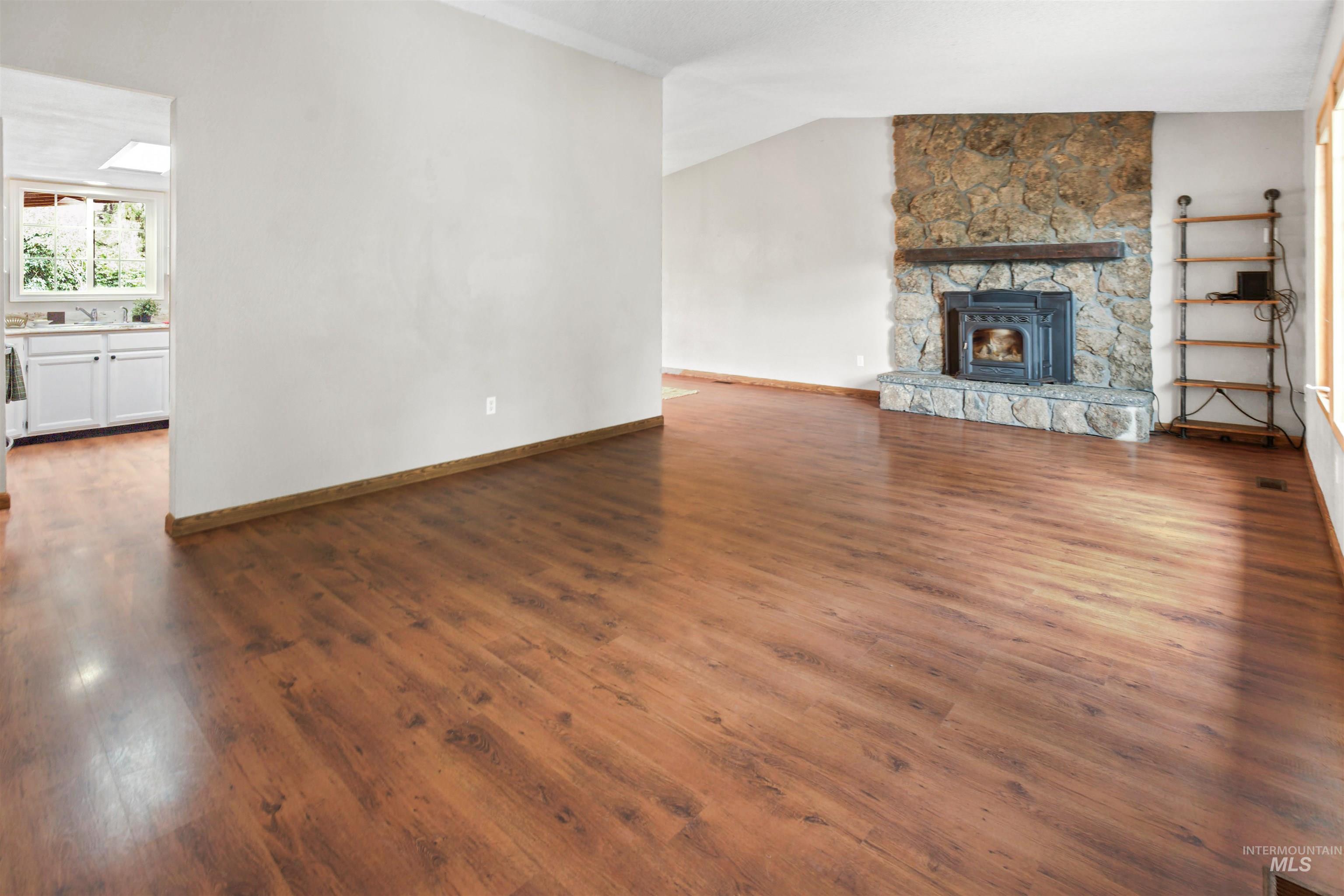 Spacious living area featuring wood-finish flooring, a stone fireplace with a wood mantel, and vaulted ceilings