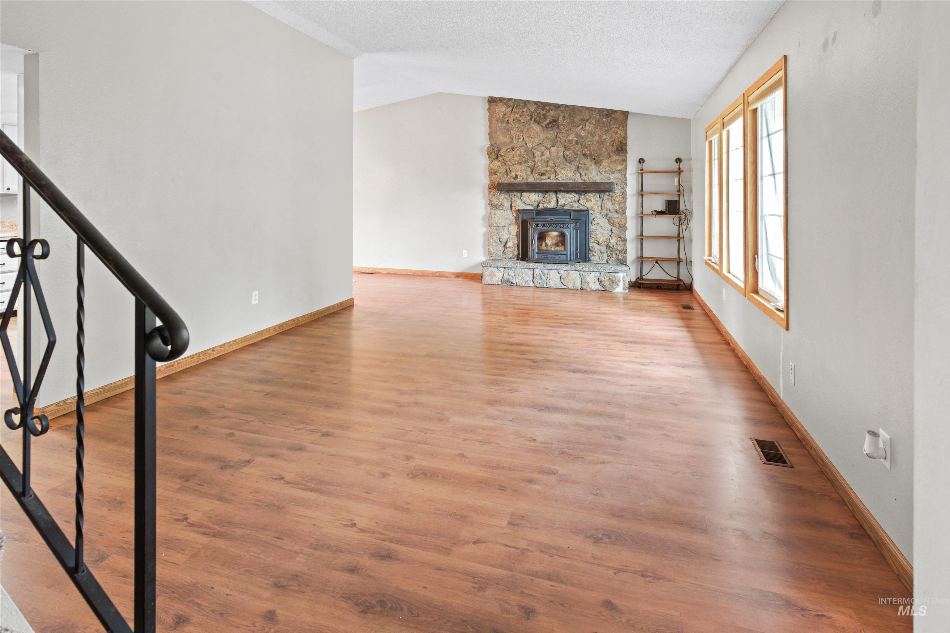 Spacious living area featuring wood-finish flooring, a vaulted ceiling, and a stone fireplace with a wood-burning insert