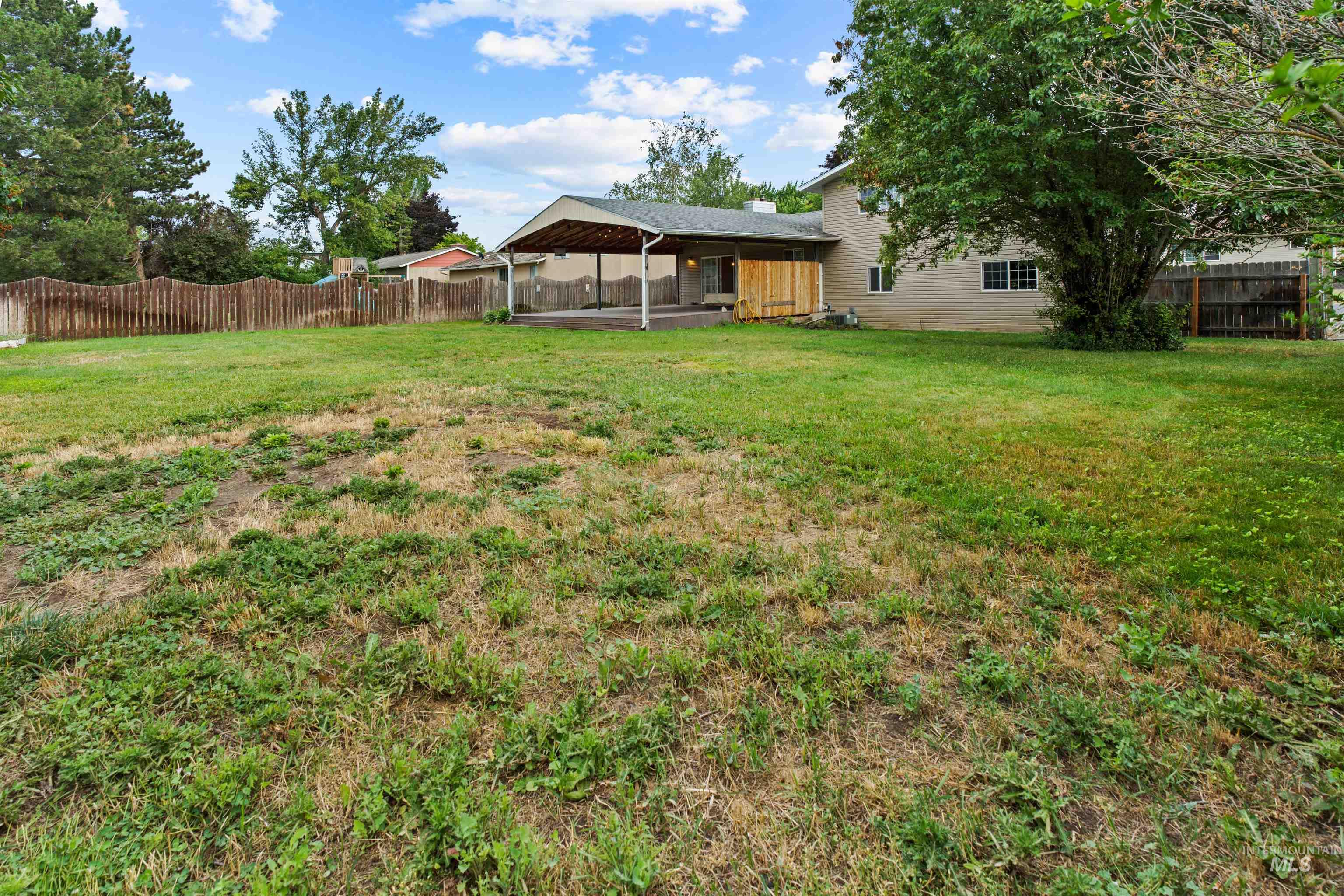 Spacious backyard featuring a covered patio structure, mature trees, and a privacy fence