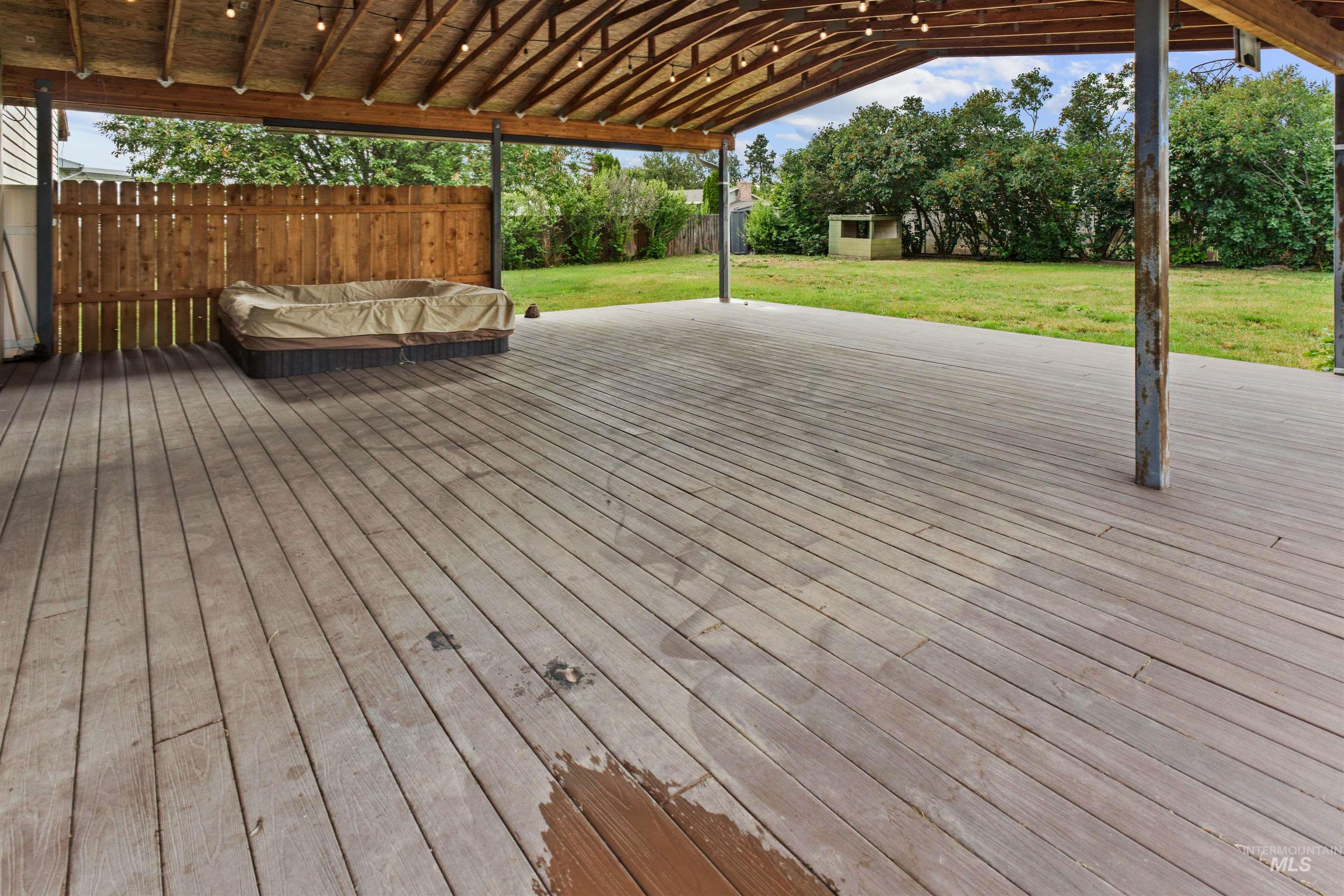 Expansive covered deck featuring wood-finish flooring, exposed beam ceiling, and string lighting
