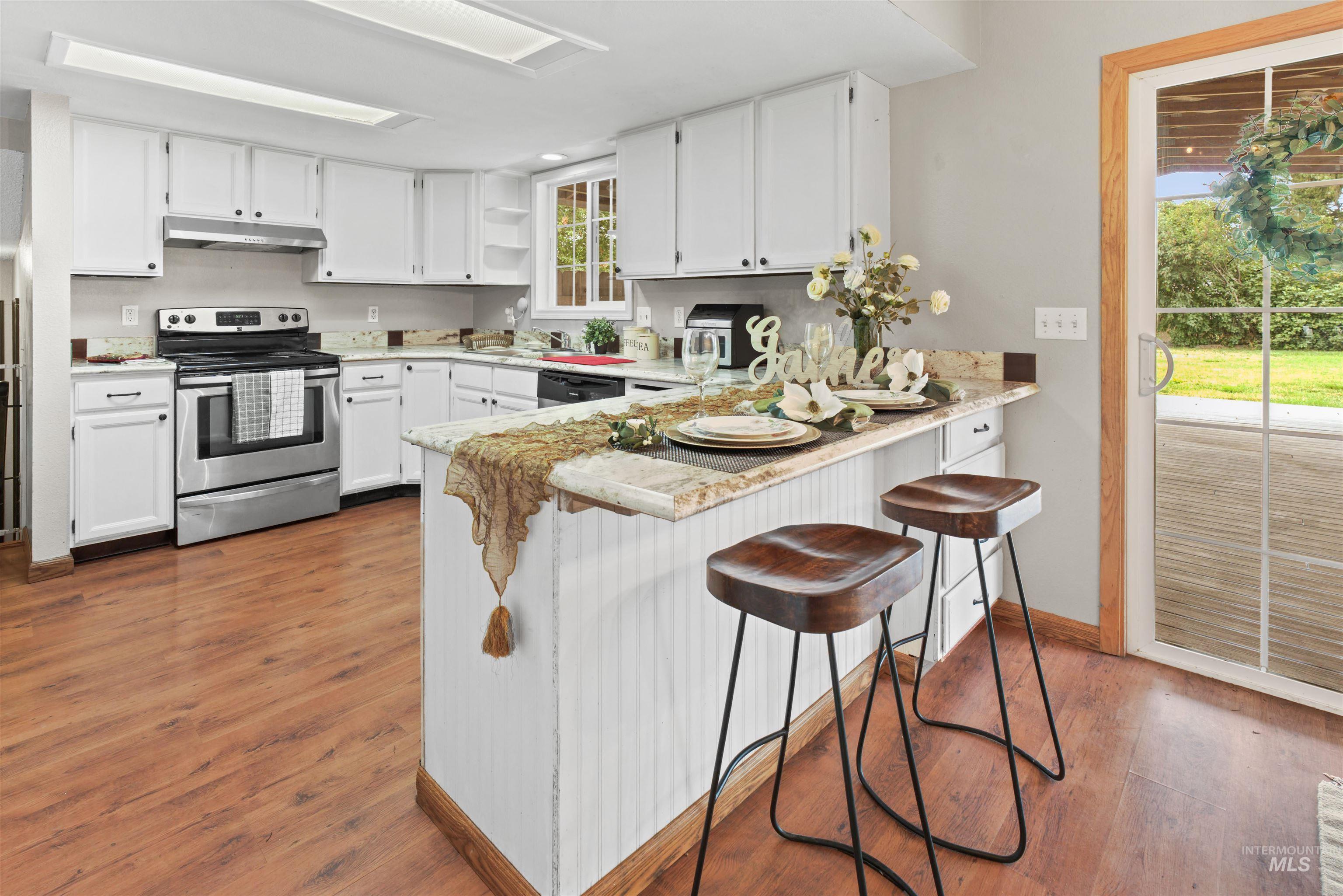 Kitchen featuring white cabinetry, light-toned countertops, wood-finish flooring, stainless steel range with overhead microwave, and a glass sliding door