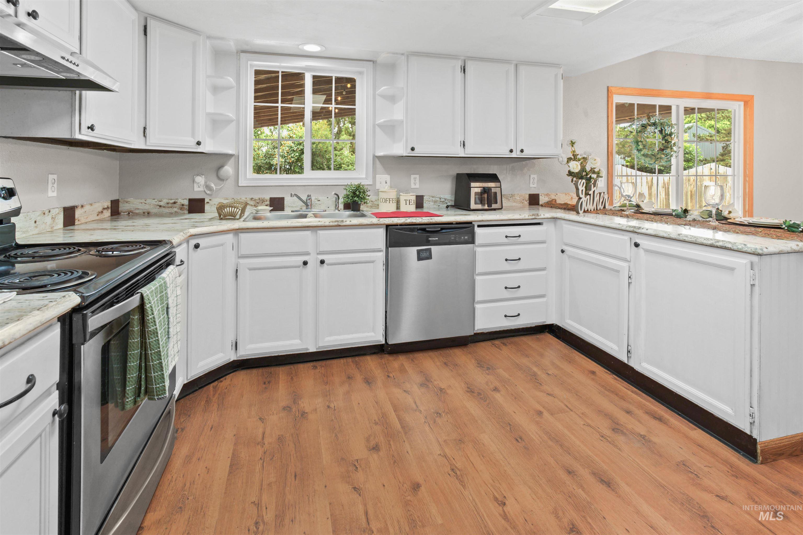 Kitchen featuring white cabinetry, granite-style countertops, wood-finish flooring, stainless steel appliances, and a skylight