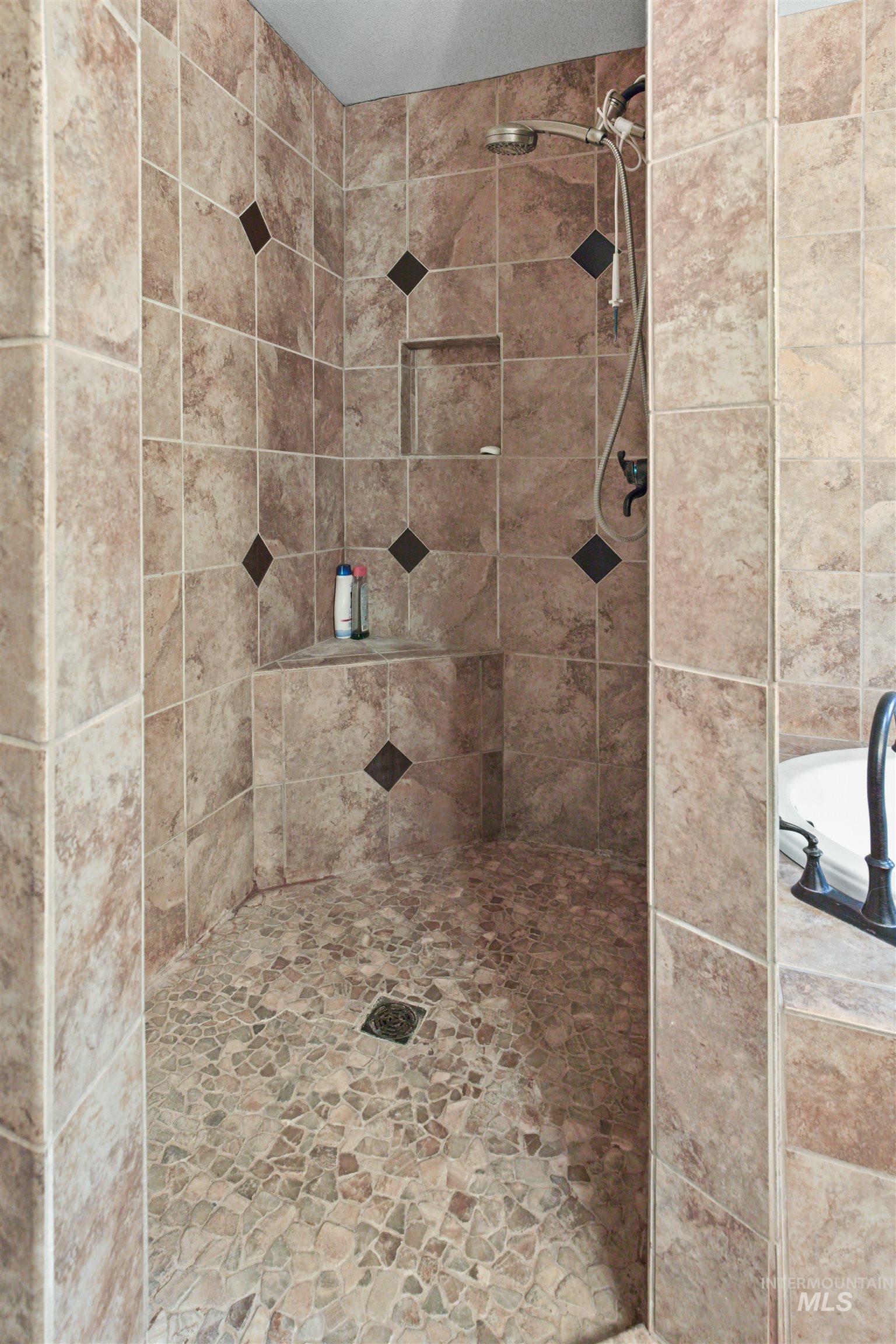 Tiled shower enclosure featuring a handheld showerhead, built-in corner bench, and recessed wall niche