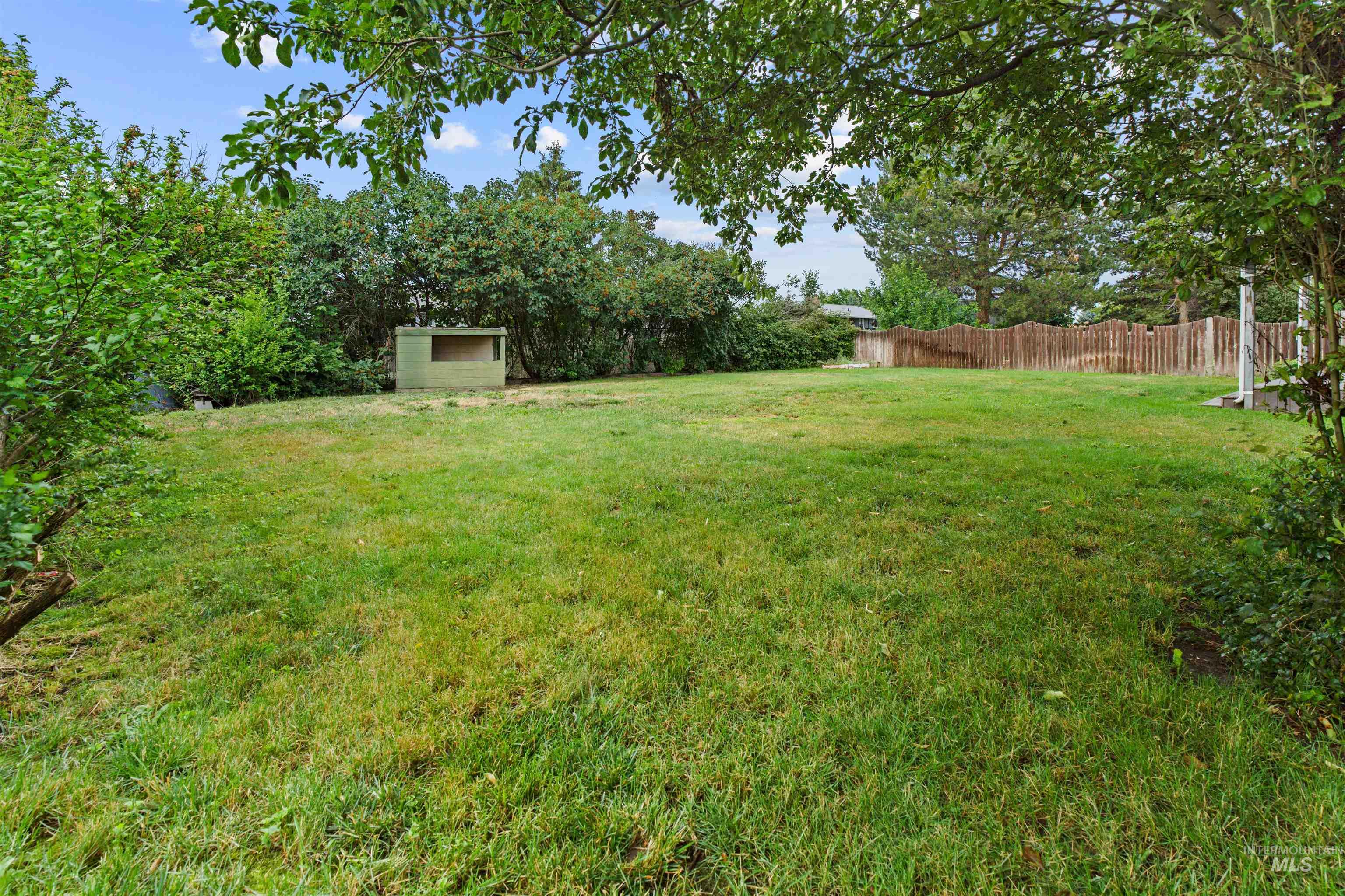 Expansive grassy yard area featuring a light green wooden shed and perimeter fencing