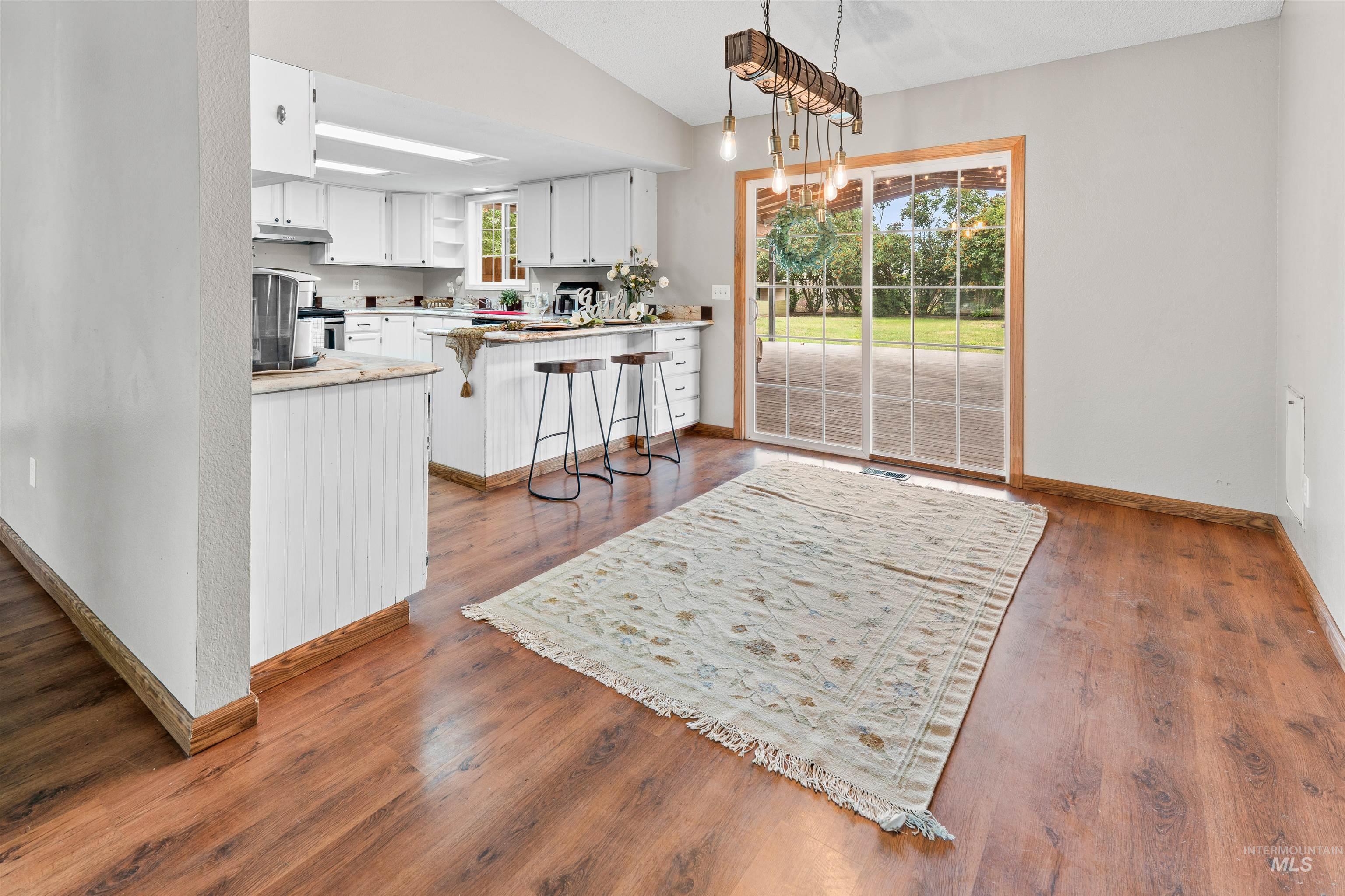 Kitchen and dining area featuring wood-finish flooring, white cabinetry, a kitchen island with beadboard paneling, and a vaulted ceiling
