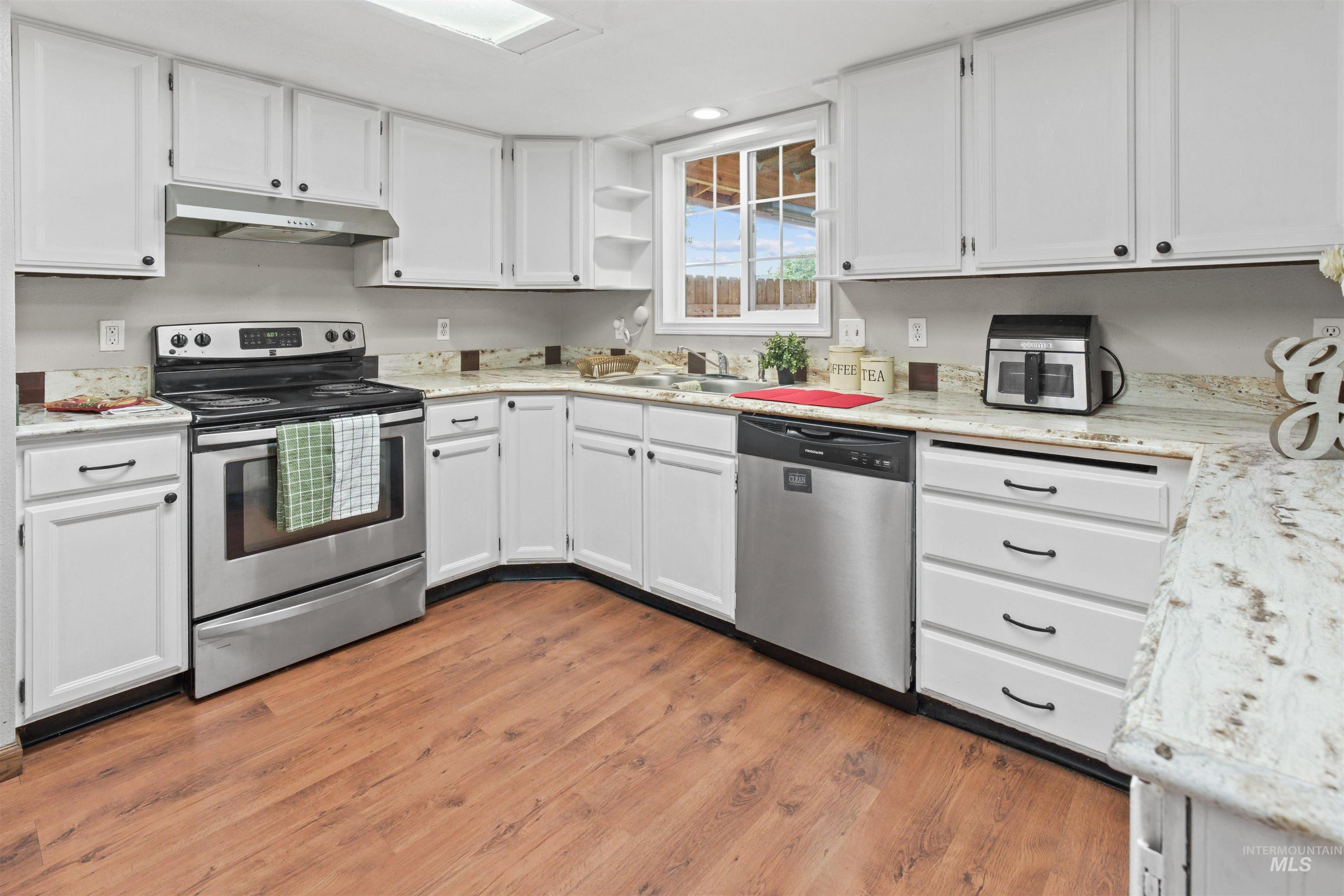 Kitchen featuring white cabinetry, granite-finish countertops, stainless steel appliances, wood-finish flooring, and a window above the sink