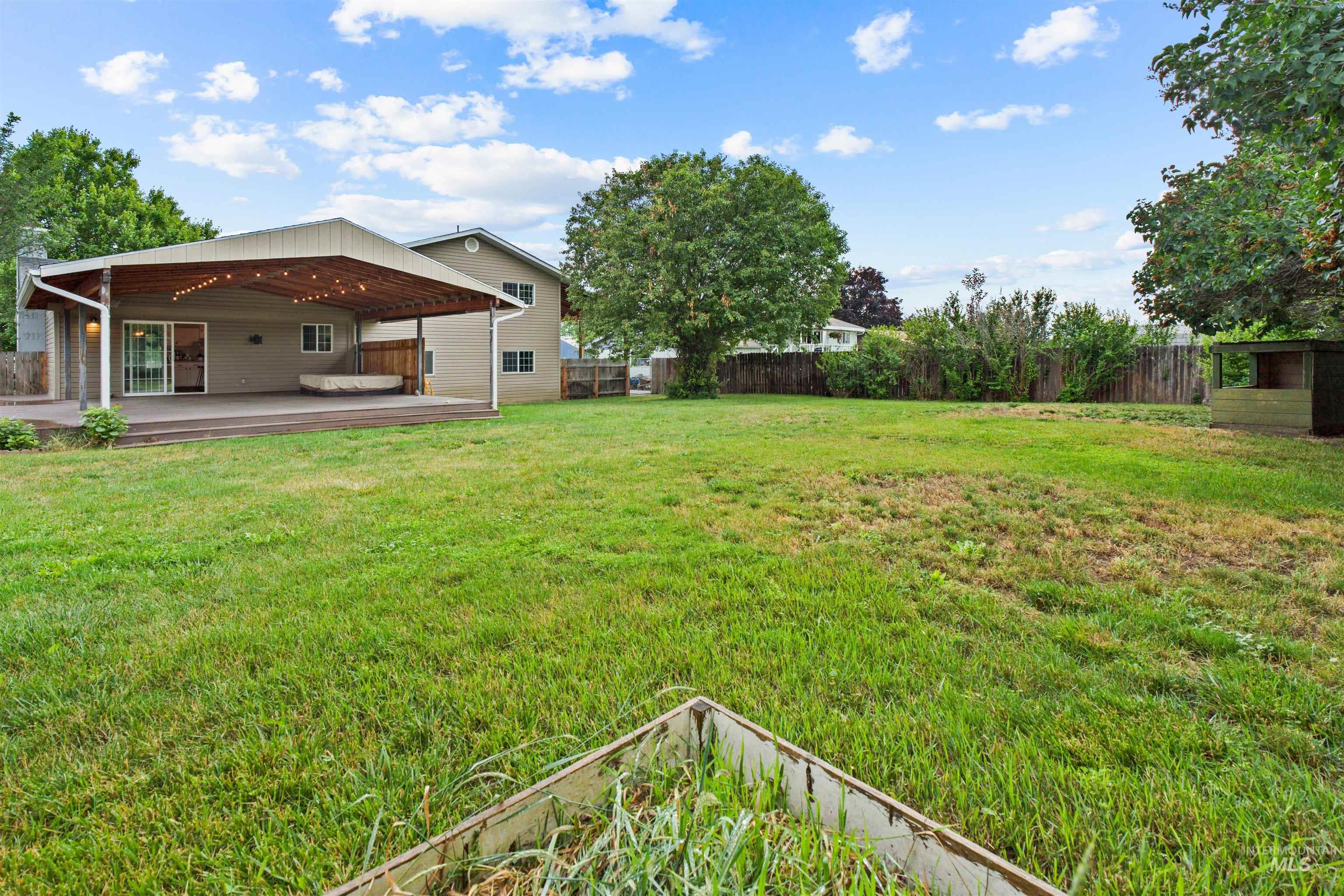 Spacious backyard featuring a covered patio with string lighting, a large wooden deck, and mature perimeter trees