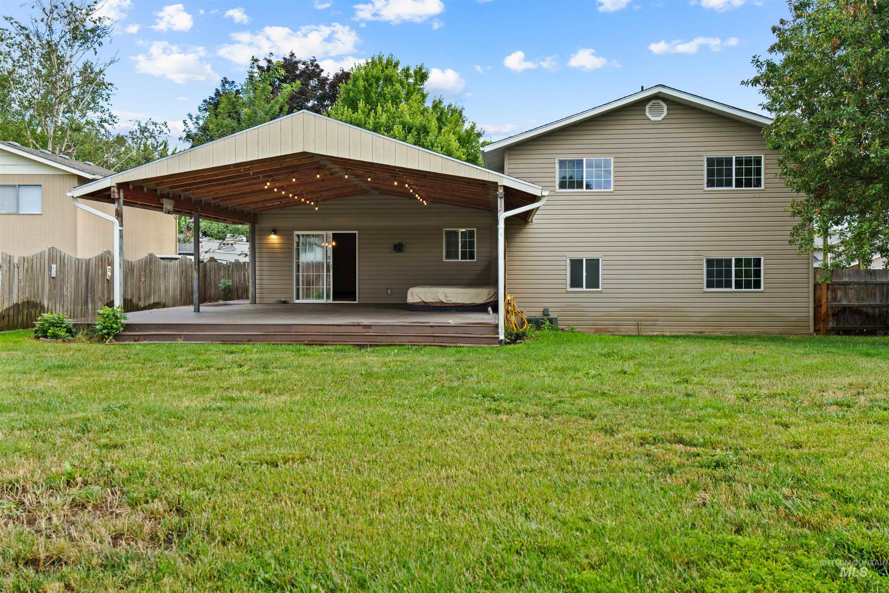 Expansive backyard featuring a large covered deck with string lighting, direct sliding door access to the interior, and a wood privacy fence