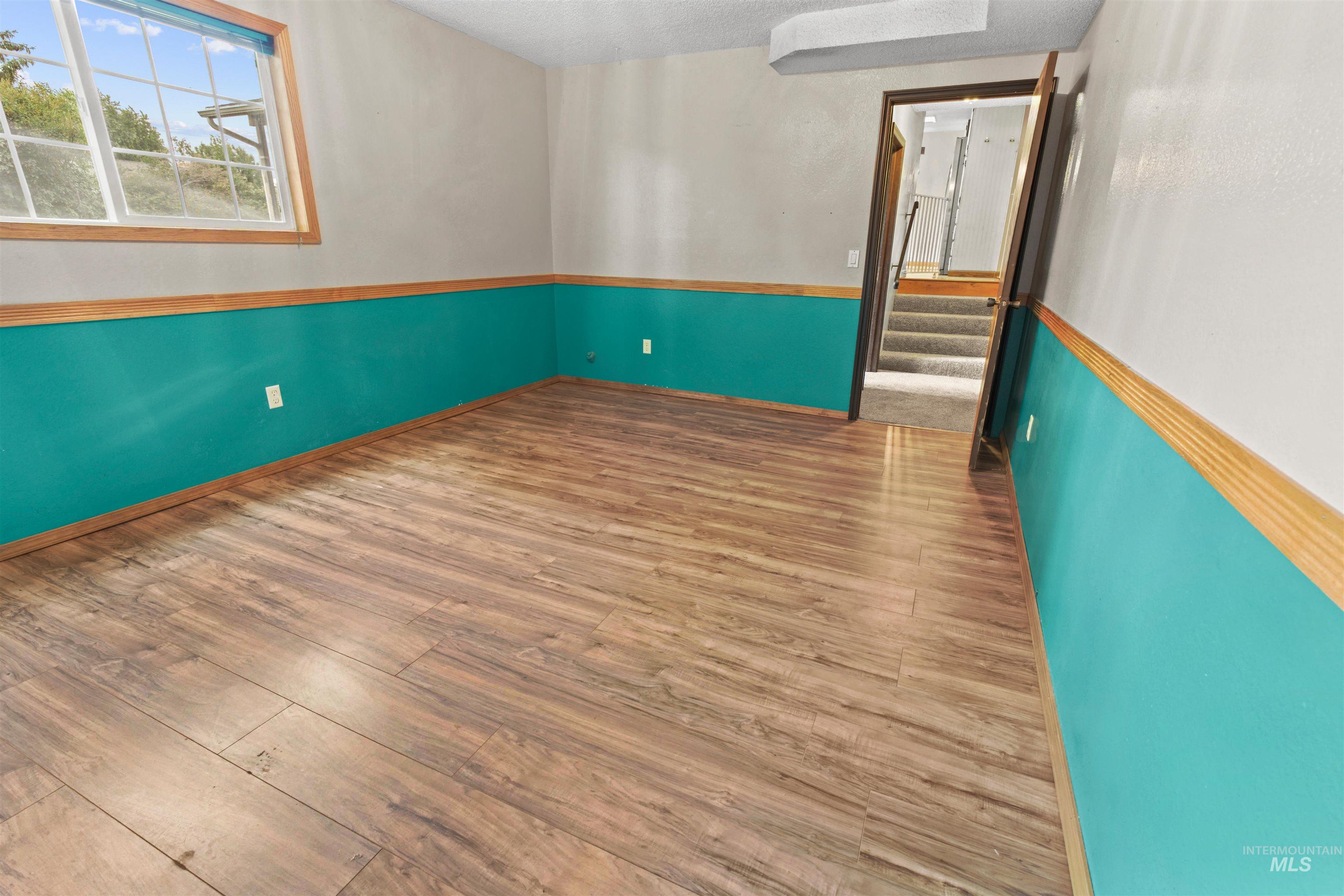Spacious room featuring wood-finish flooring, a window with wood trim, and a two-tone wall treatment