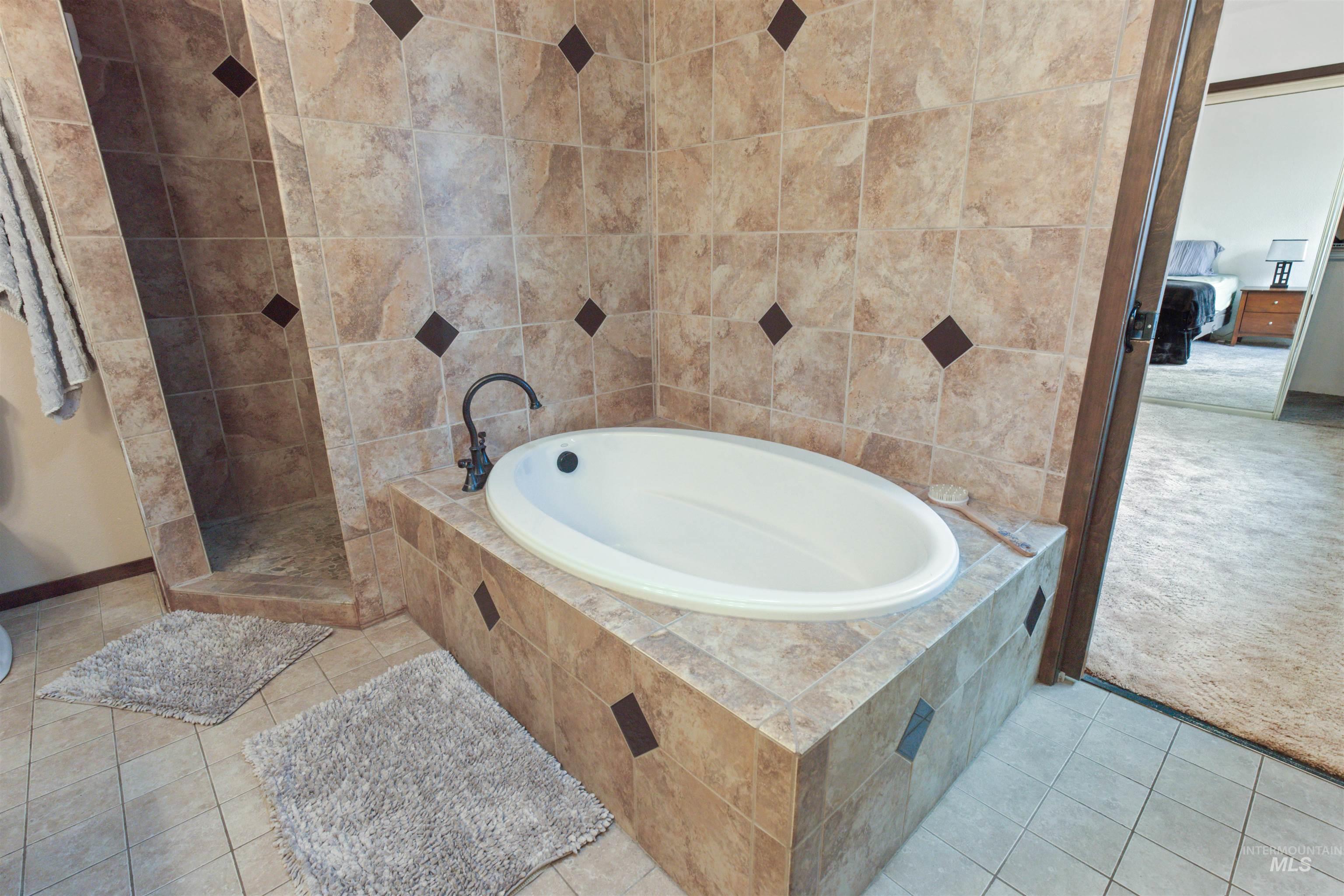 Built-in soaking tub with a dark bronze faucet, surrounded by neutral-toned tile with accent inlays