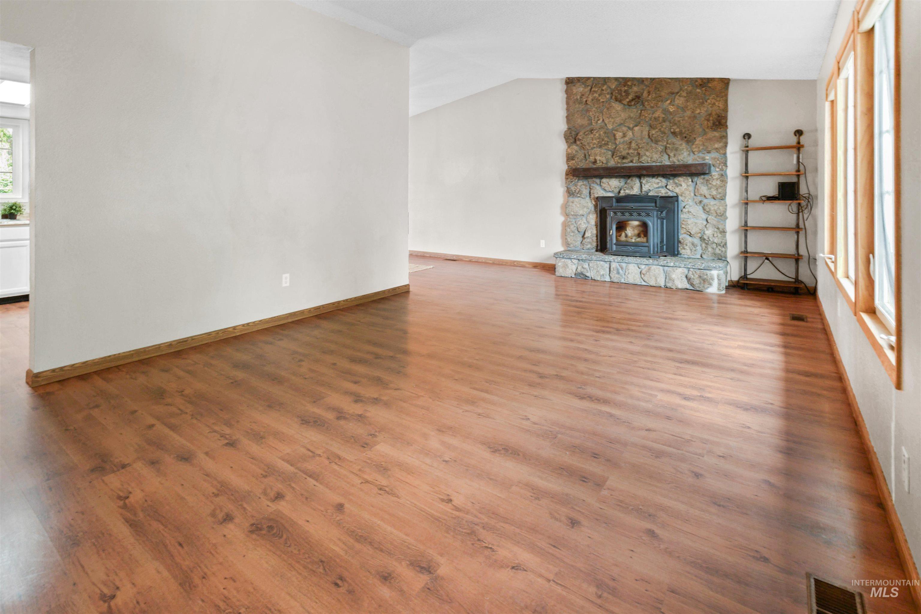 Spacious room featuring wood-finish flooring, a stone-clad fireplace with a wood-burning insert, and multiple windows providing natural illumination