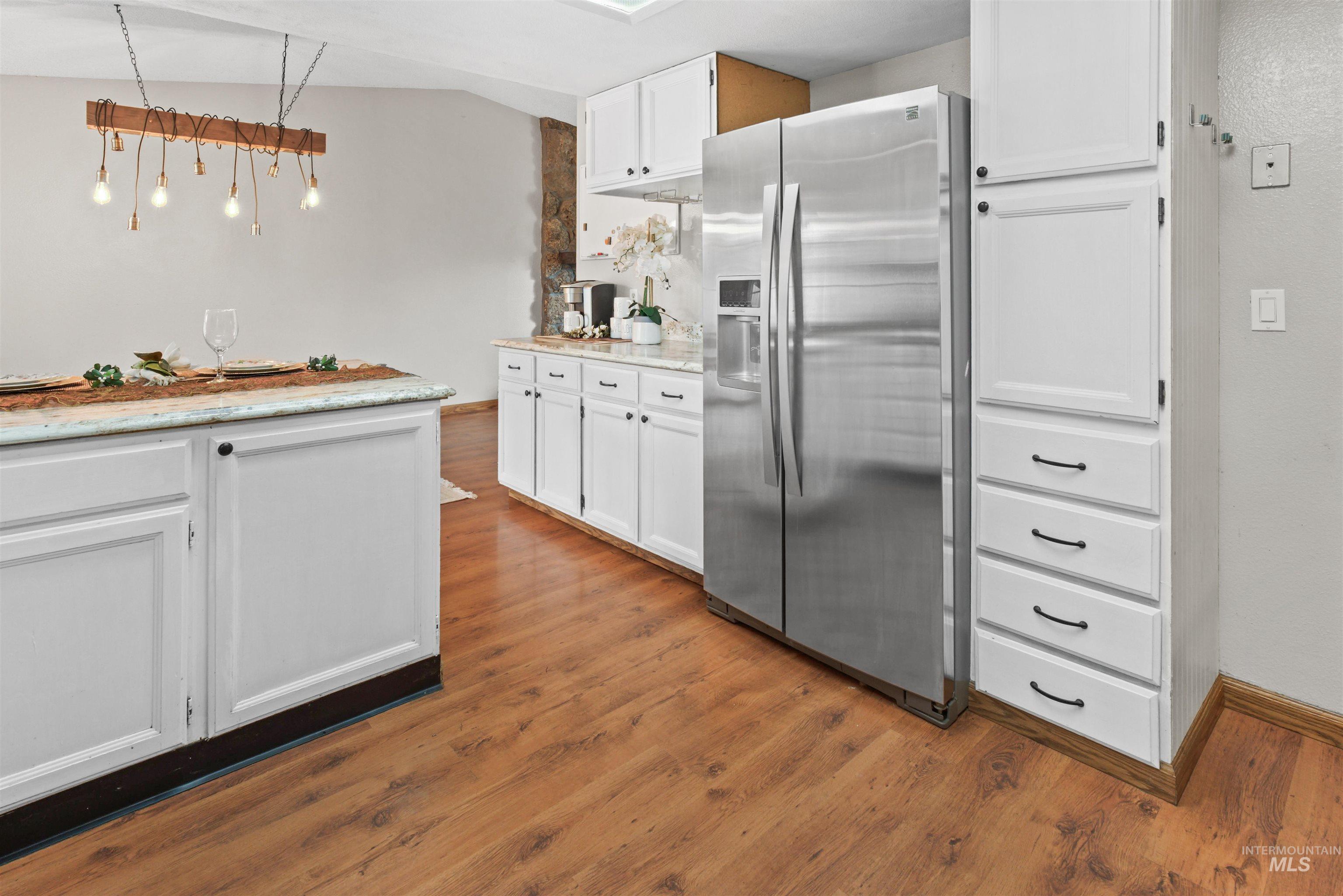 Kitchen featuring wood-finish flooring, white cabinetry with dark hardware, stainless steel side-by-side refrigerator, white countertops, and a skylight