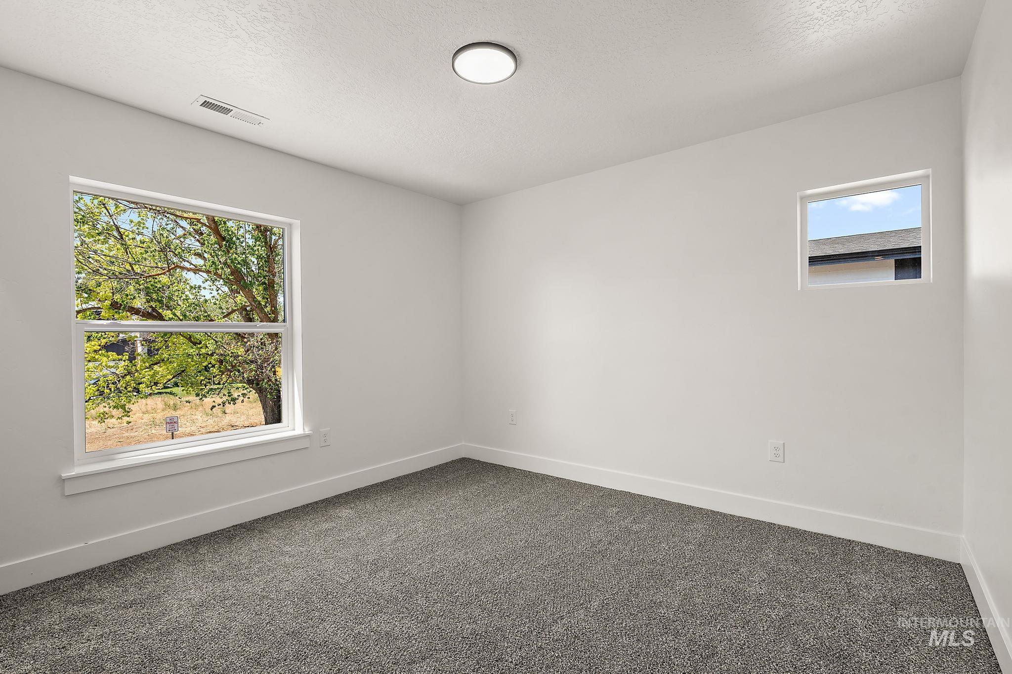 Empty room with plenty of natural light, dark colored carpet, and a textured ceiling