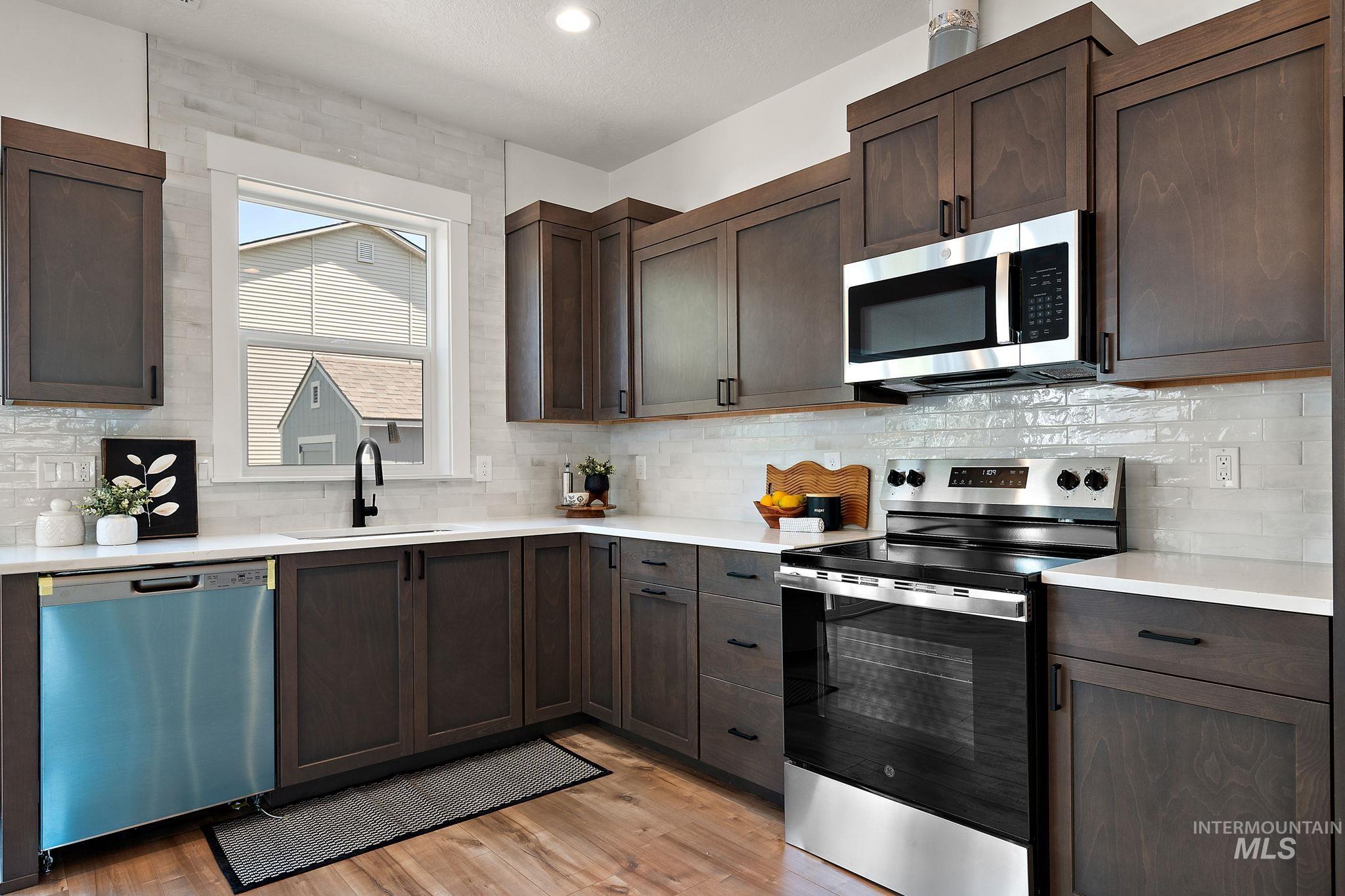 Kitchen featuring stainless steel appliances, light countertops, light wood-style flooring, and dark brown cabinets
