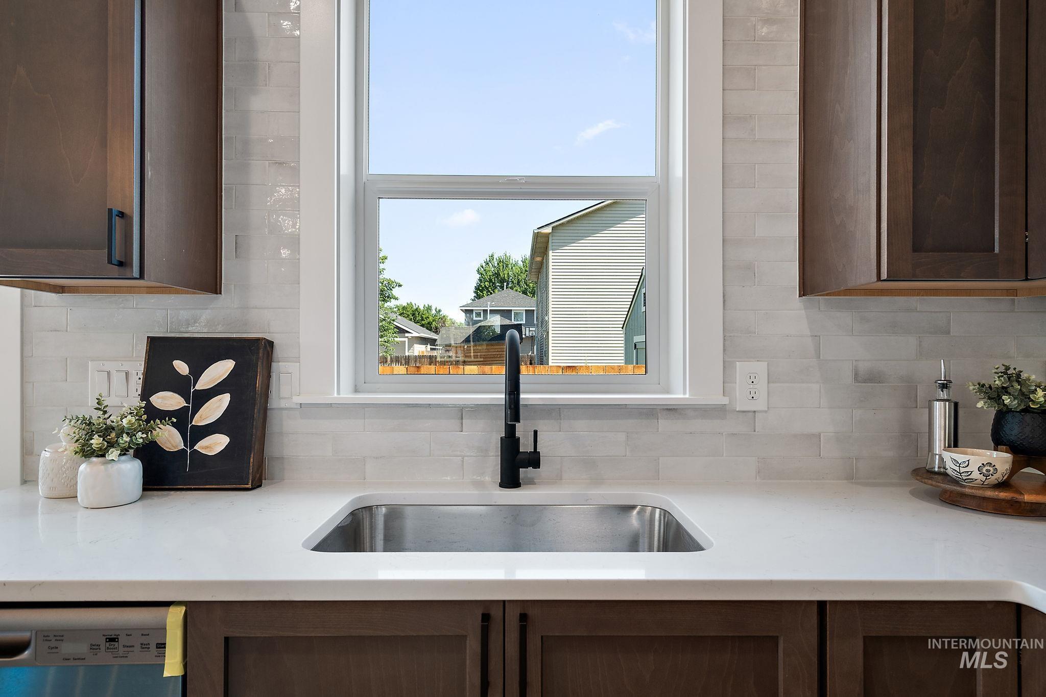 Kitchen featuring stainless steel dishwasher, backsplash, light countertops, and dark brown cabinets