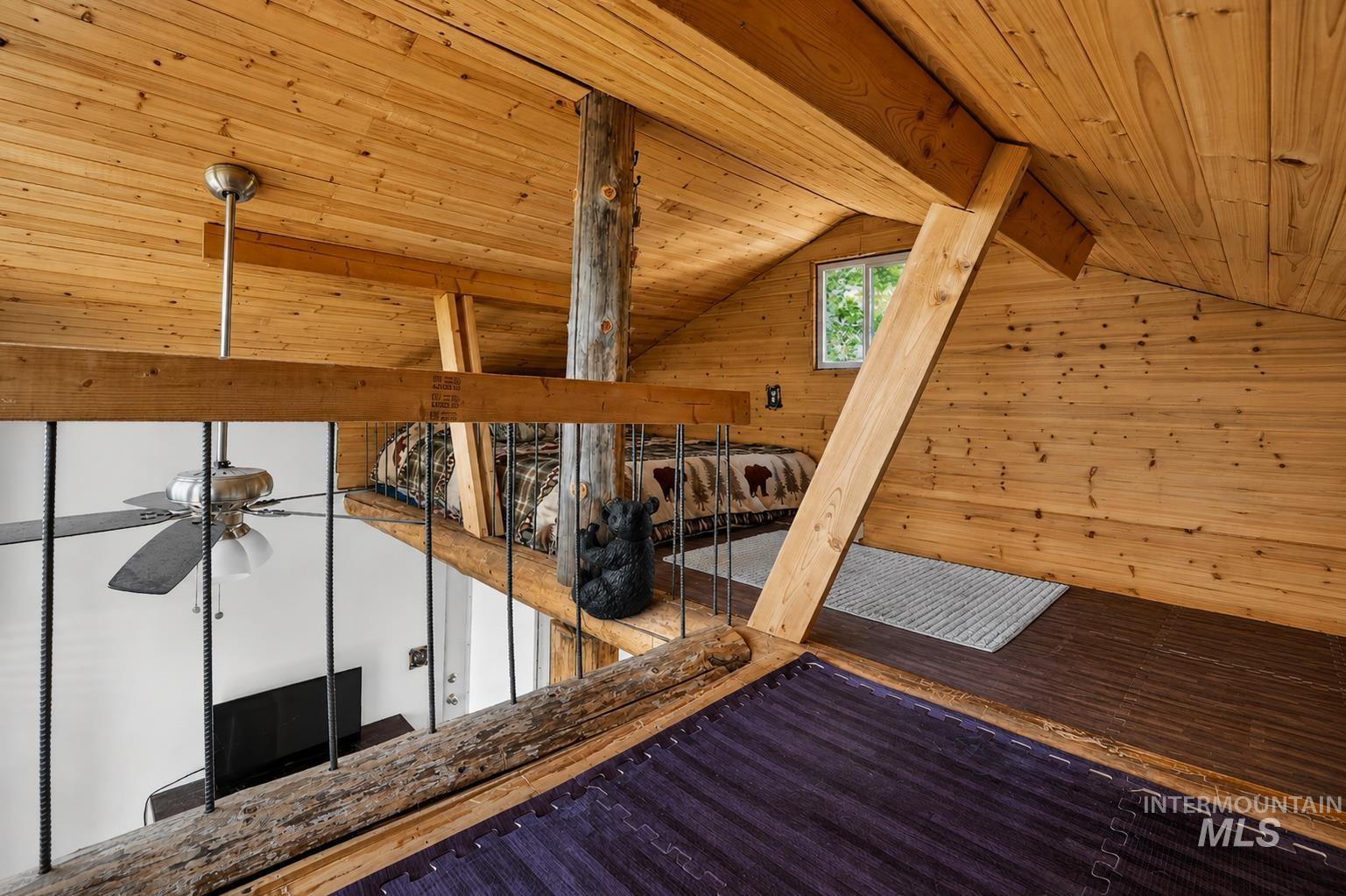 Loft space featuring natural wood paneling throughout, exposed wood beams, and a window providing natural light